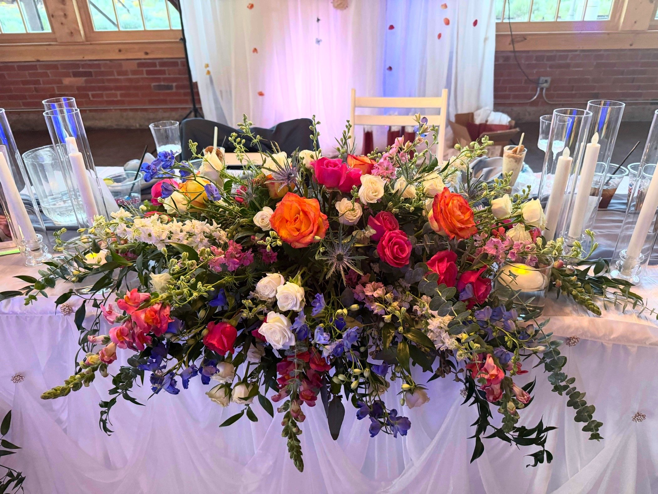 A large floral centerpiece with multicolored flowers on a decorated table at a celebration event.