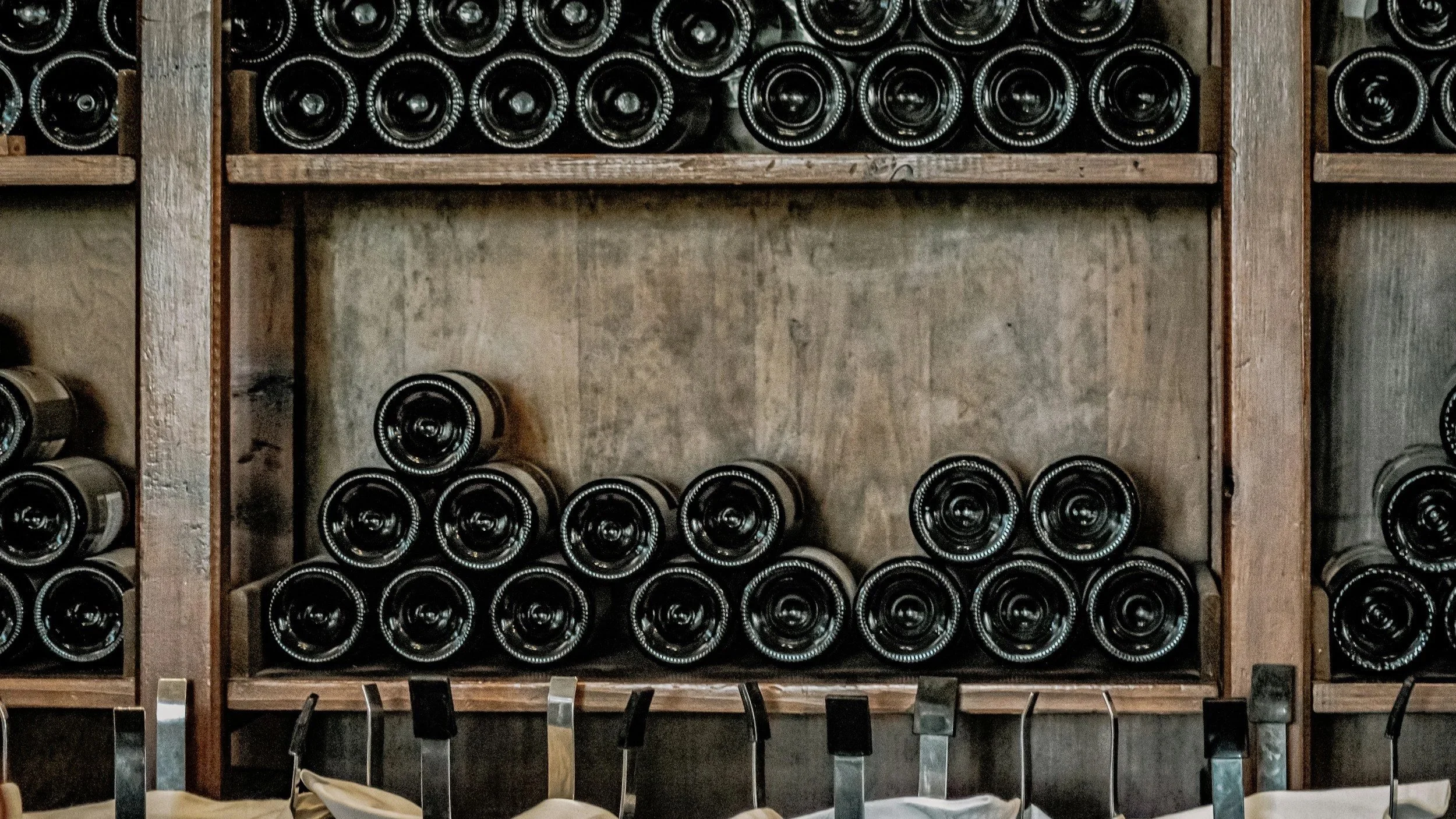 Wine bottles stored horizontally on wooden shelves in a wine cellar or store.