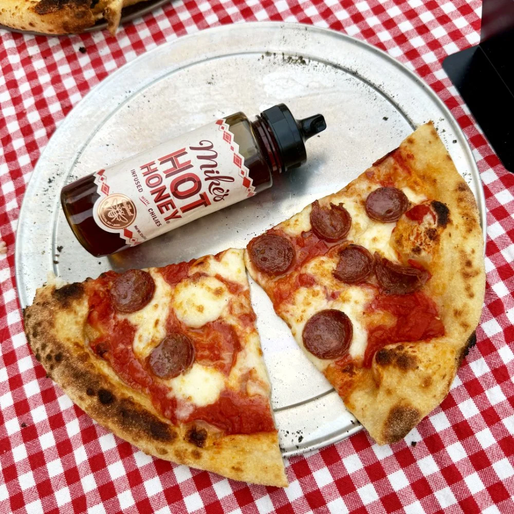 A pepperoni pizza by Soci pizza on a table with a bottle of hot honey in North Carolina.
