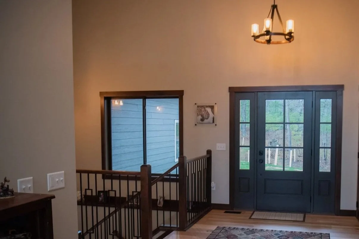 Entryway with double front doors, staircase railing, large window, and chandelier lighting in a modern craftsman home.
