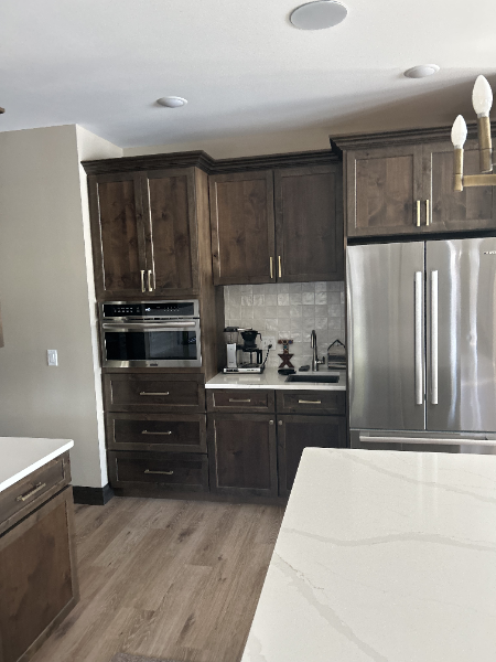 Modern kitchen with dark wood cabinetry, built-in oven and microwave, stainless steel refrigerator, and quartz countertops.