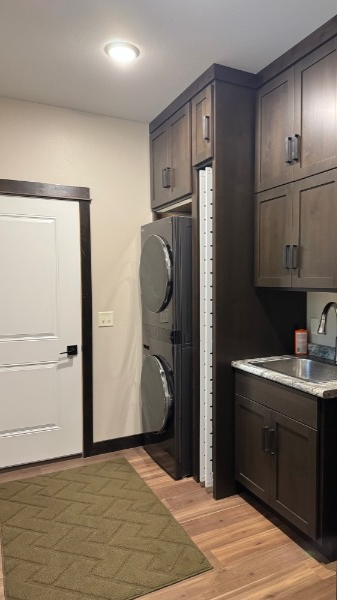 Custom laundry room with stacked washer and dryer, built-in dark wood cabinetry, utility sink, and folding counter.