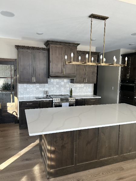 Modern kitchen with large island, dark wood cabinetry, quartz countertops, tile backsplash, and linear pendant lighting.