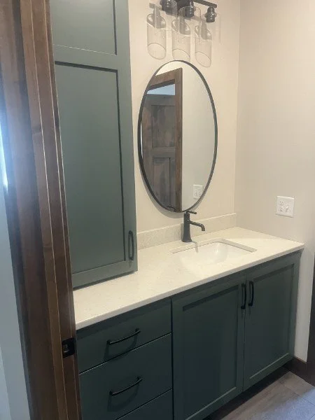 Modern bathroom vanity with round mirror, quartz countertop, and blue cabinetry with matte black fixtures.