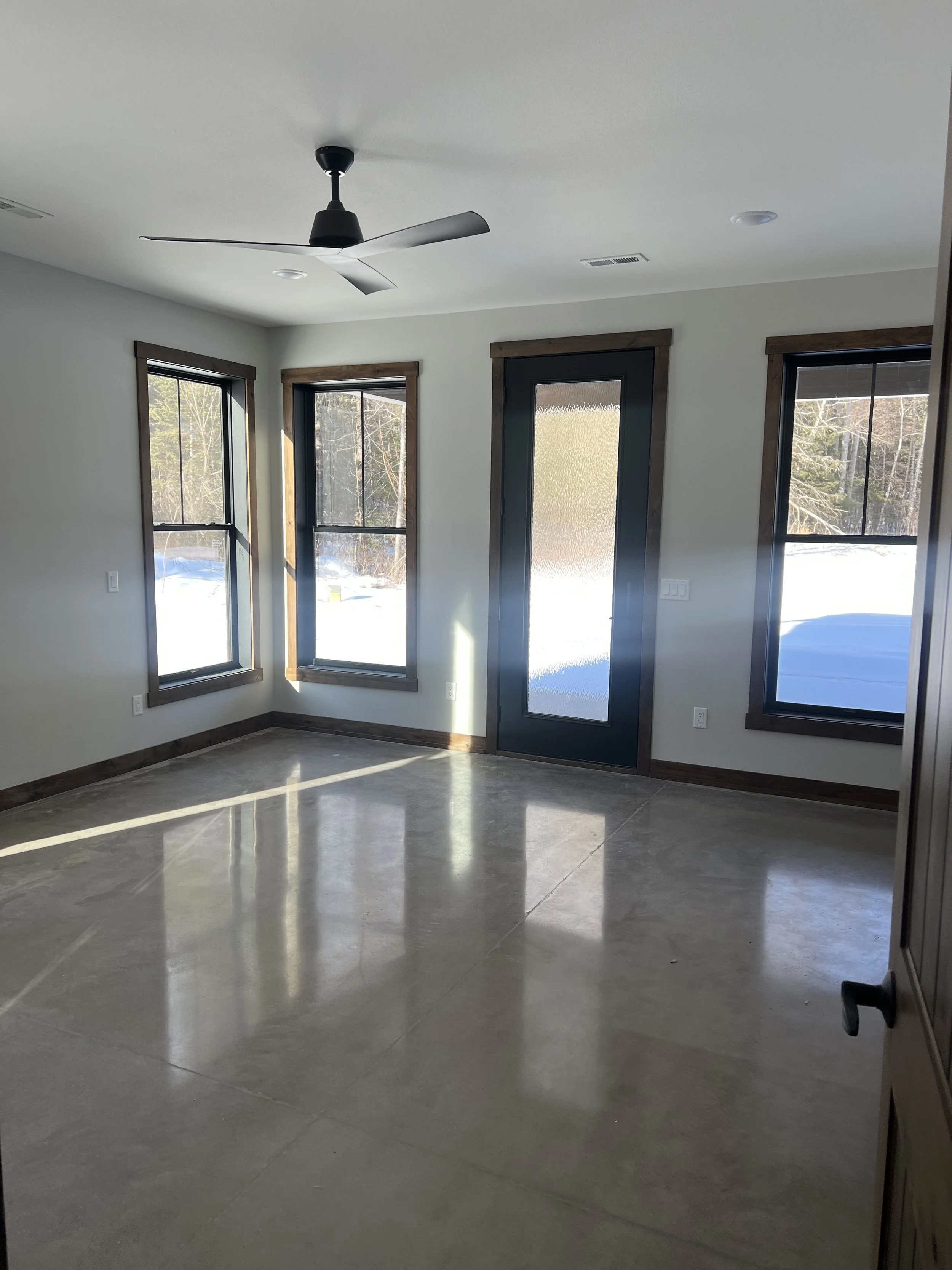 Bright bedroom with large windows, glass door to outdoor deck, ceiling fan, and polished stone flooring.