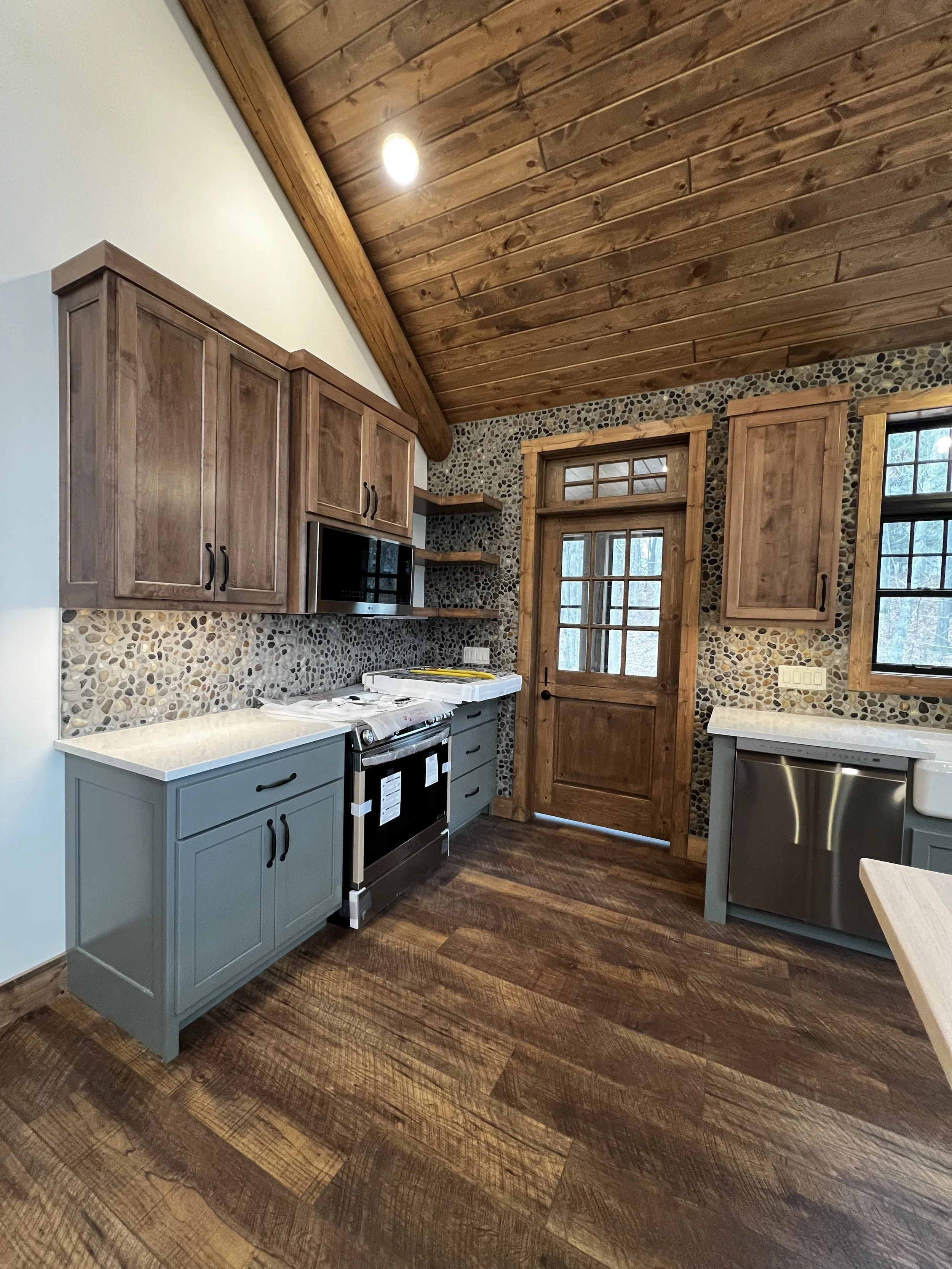 Rustic kitchen with reclaimed wood ceiling, stone backsplash, farmhouse sink, and custom cabinetry with stainless steel appliances.