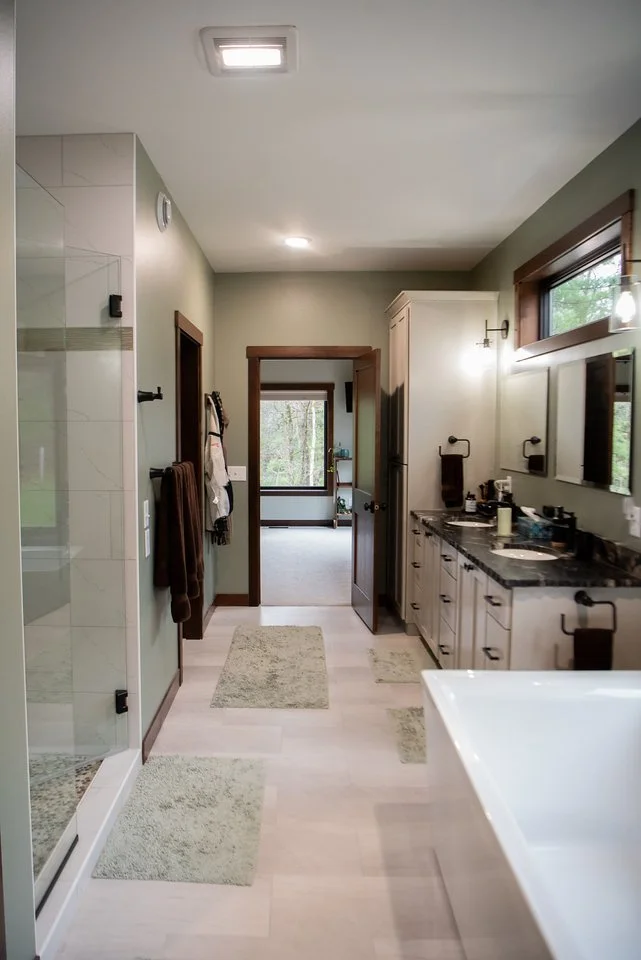 Long bathroom with double vanity, glass walk-in shower, soaking tub, and natural light from high windows.