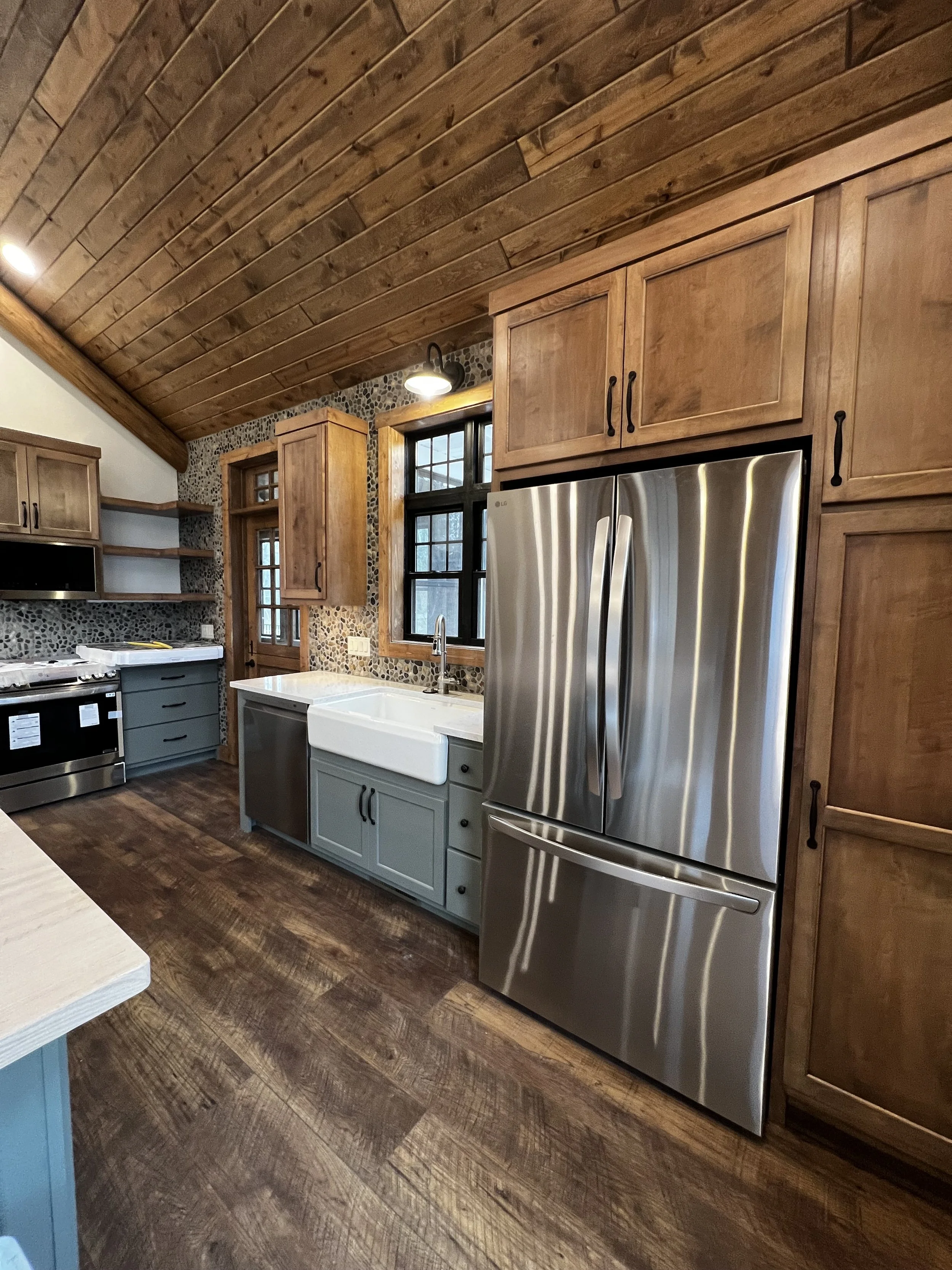 Rustic kitchen with wood plank ceiling, farmhouse sink, stainless steel refrigerator, and custom wood cabinetry.