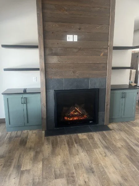 Modern fireplace with wood accent wall, built-in shelving, and green cabinetry on either side.
