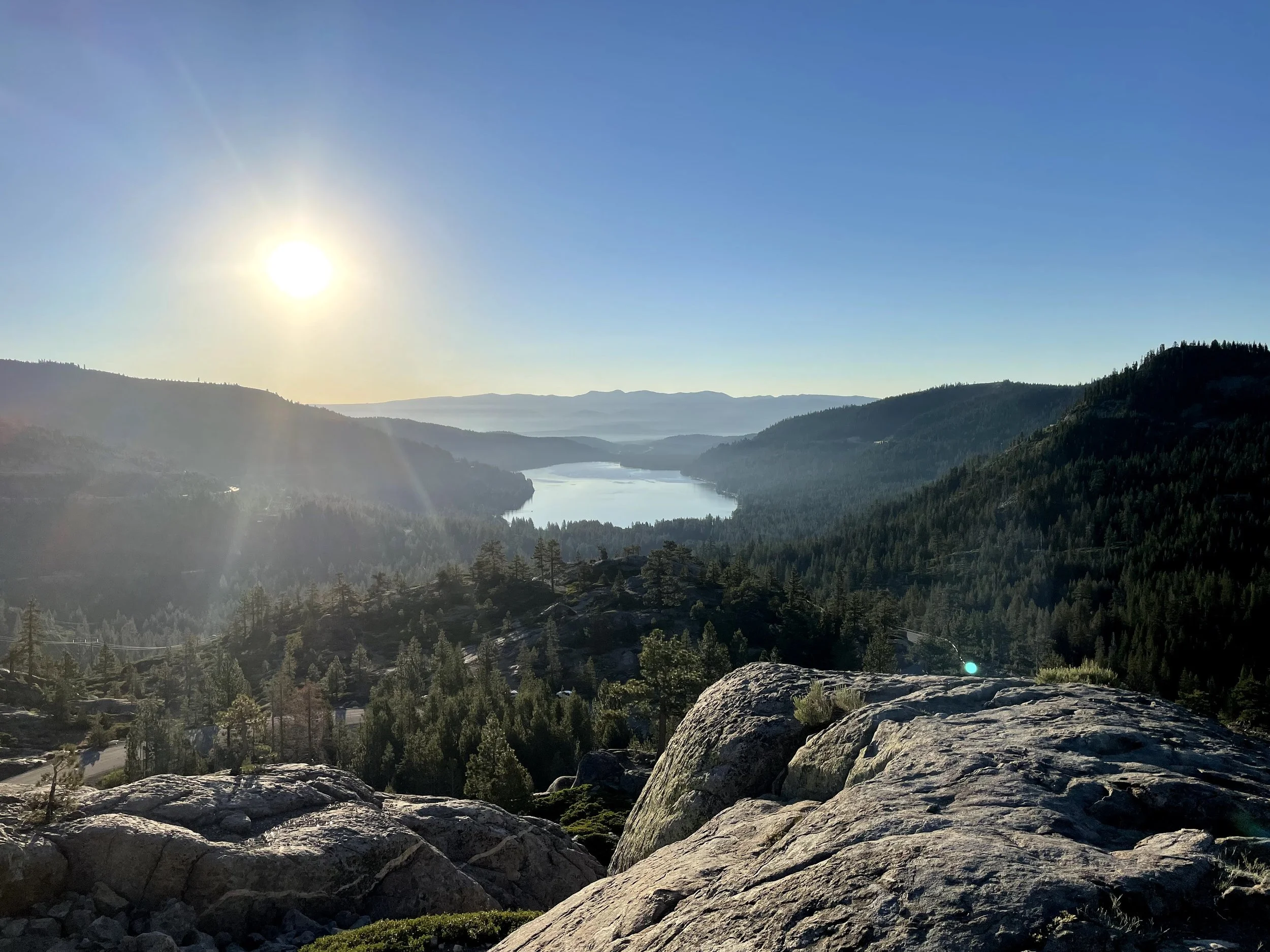 Scenic view of a river winding through forested mountains under a clear blue sky with the sun shining brightly.