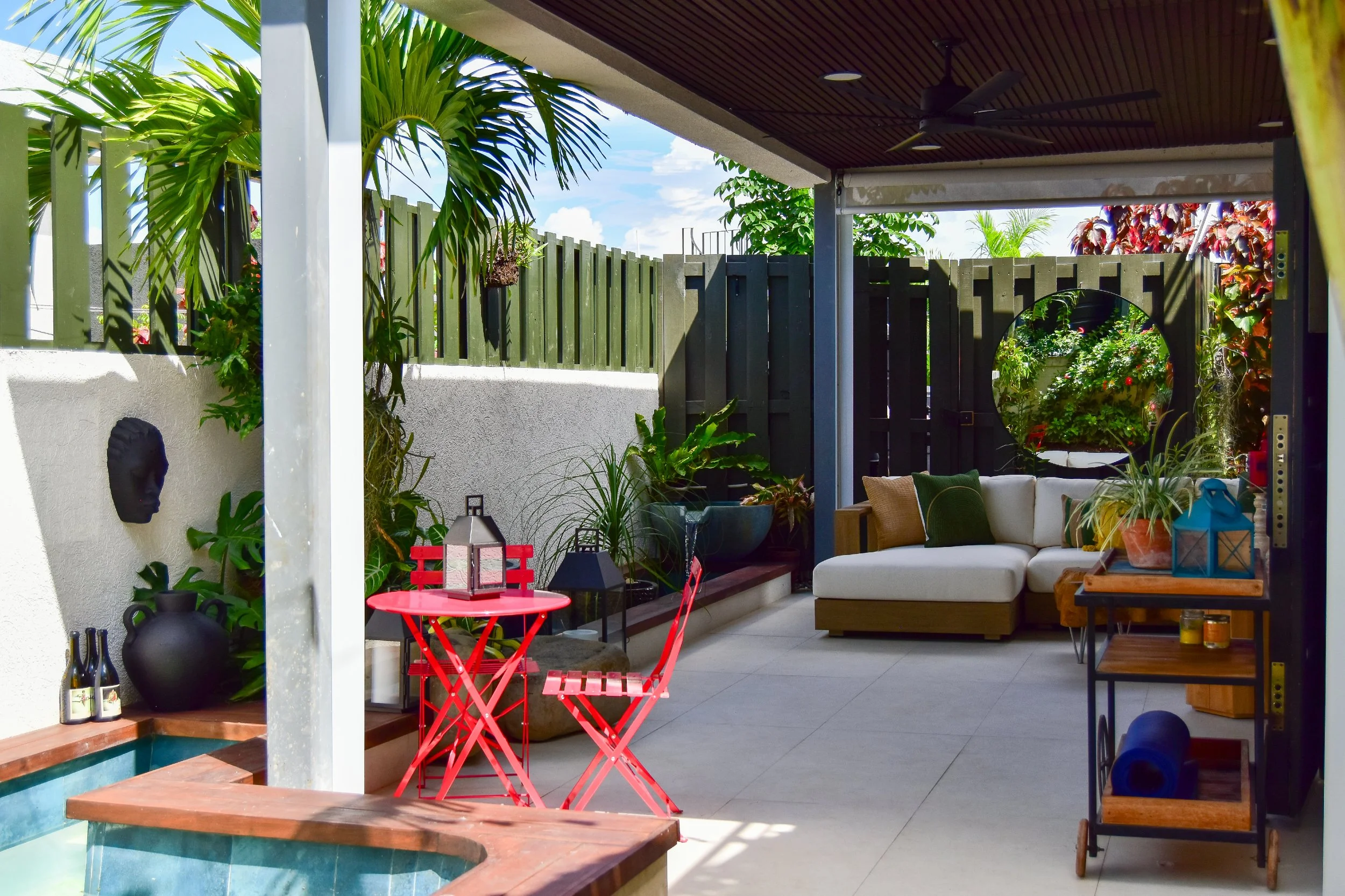 Modern backyard design featuring a tropical lounge area, plunge pool, red bistro seating, lush planting, and a stylish outdoor patio in Ocho Rios, Jamaica
