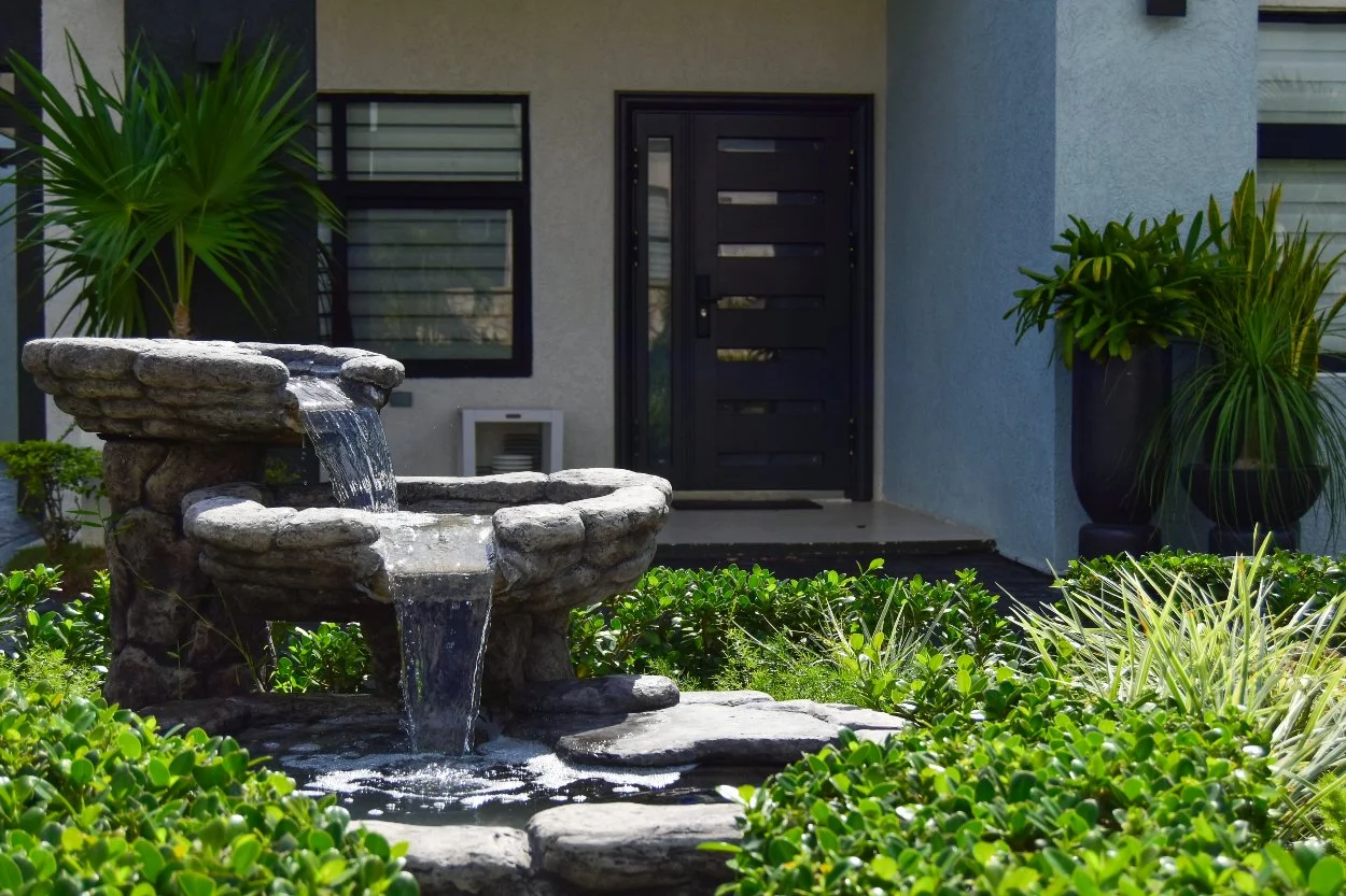 Modern tiered garden water feature with cascading water set among lush tropical planting at the entrance of a contemporary Jamaican home, designed by AurumScape.