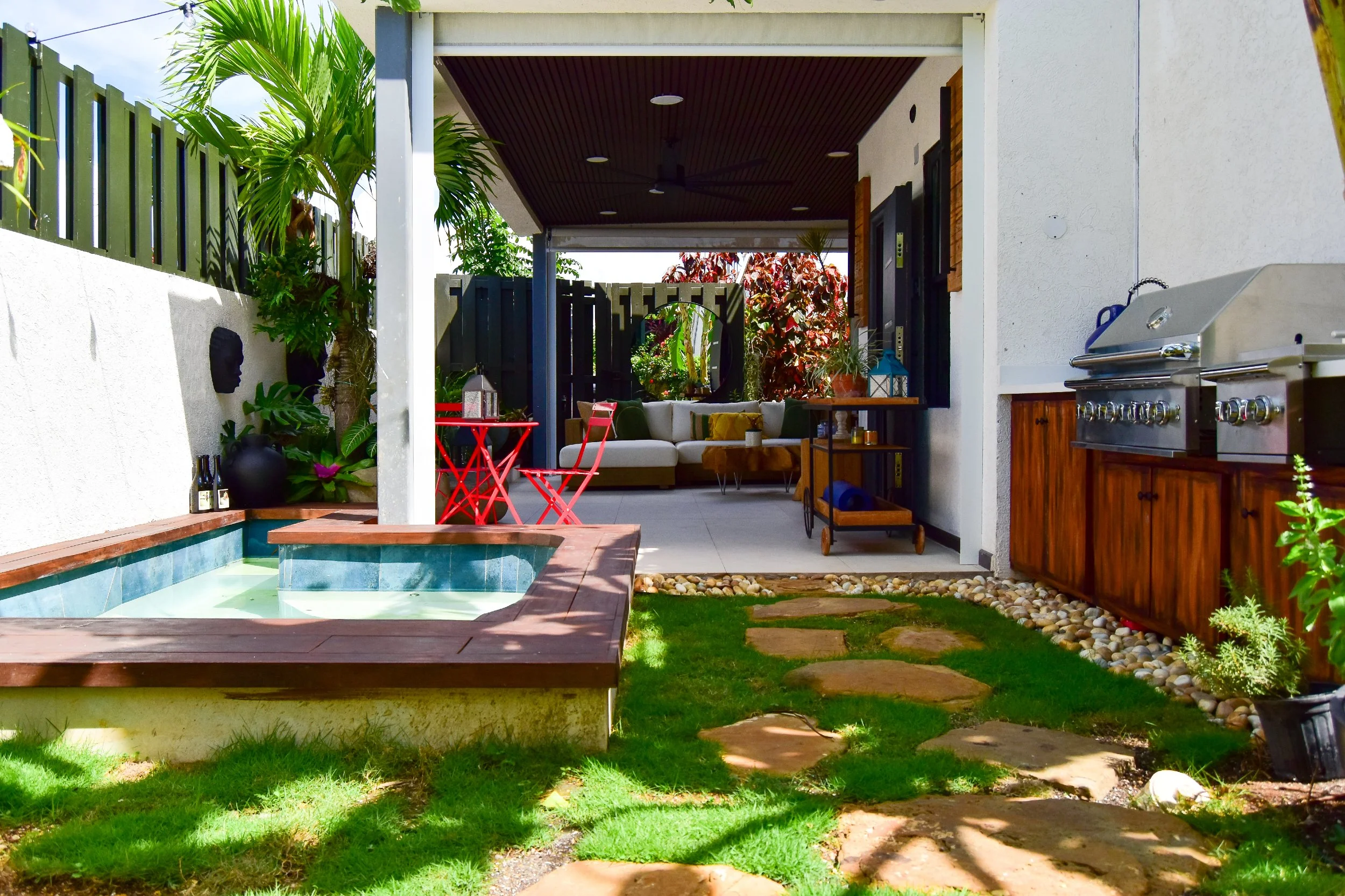 Modern backyard design featuring an in-ground jacuzzi, outdoor kitchen, shaded patio lounge, and tropical garden pathway in Ocho Rios, Jamaica.