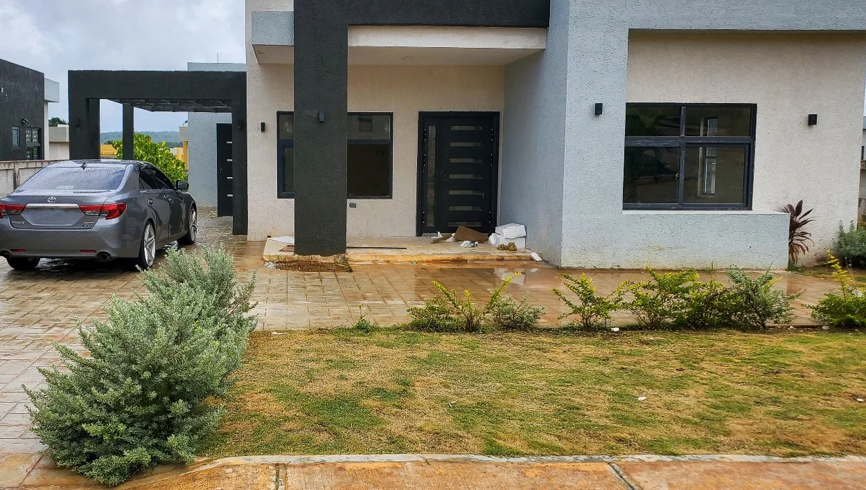 Front yard of a modern home in Jamaica before professional landscaping, with patchy grass and minimal planting.