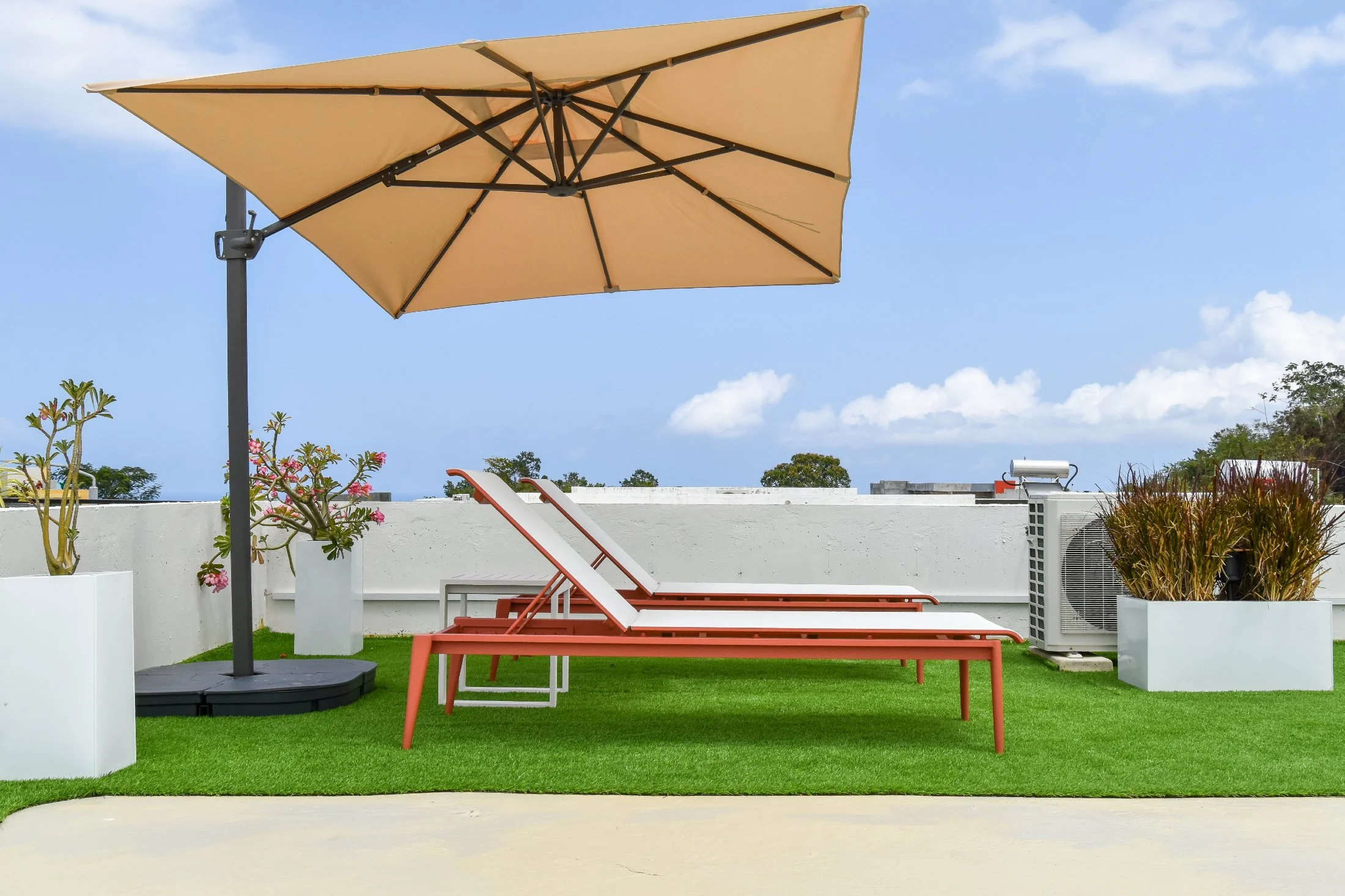 Modern rooftop garden terrace featuring two lounge chairs, a large umbrella, tropical potted plants, and artificial turf, styled for outdoor living in Jamaica.