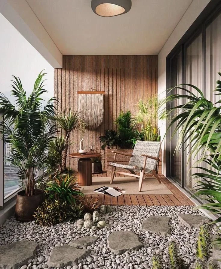 Modern balcony garden design with tropical plants, pebble flooring, wooden decking, and a woven outdoor lounge chair creating a serene small-space retreat in Jamaica.