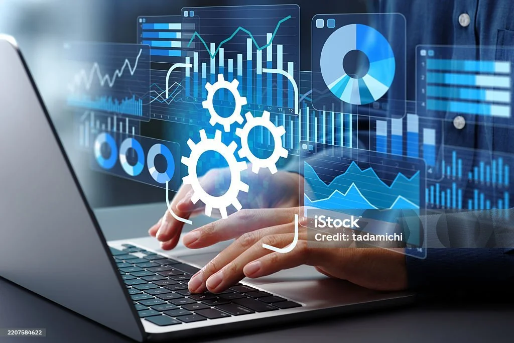 A person using a laptop with digital charts, graphs, and gear icons overlaid, representing data analysis and technology.