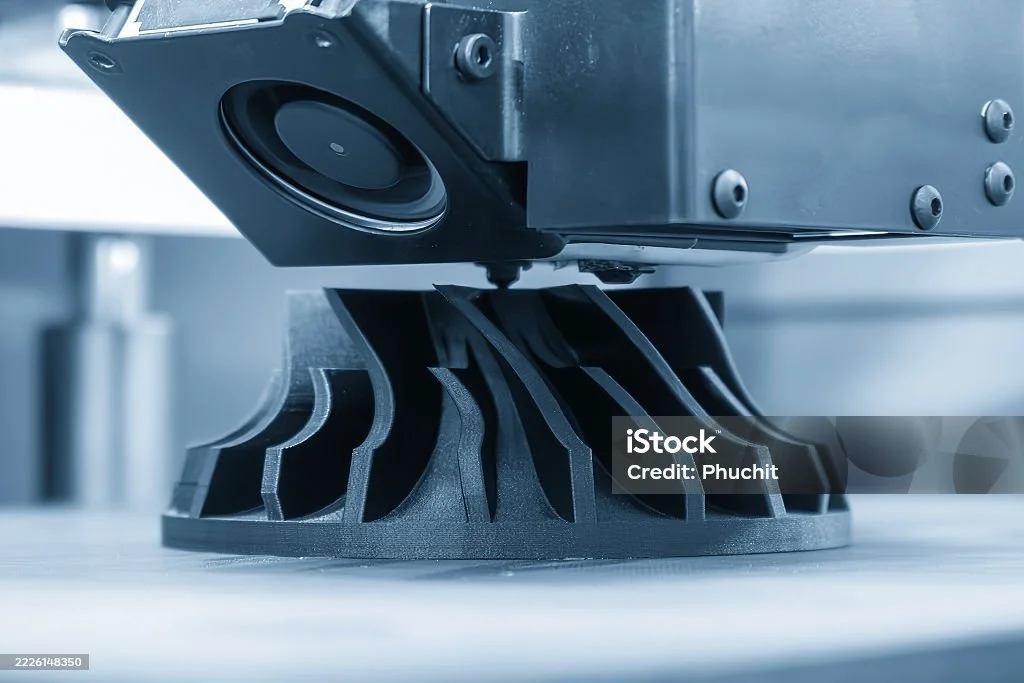 Close-up of a 3D printer nozzle extruding material onto a print bed, with a focus on the mechanical components and layered structure.
