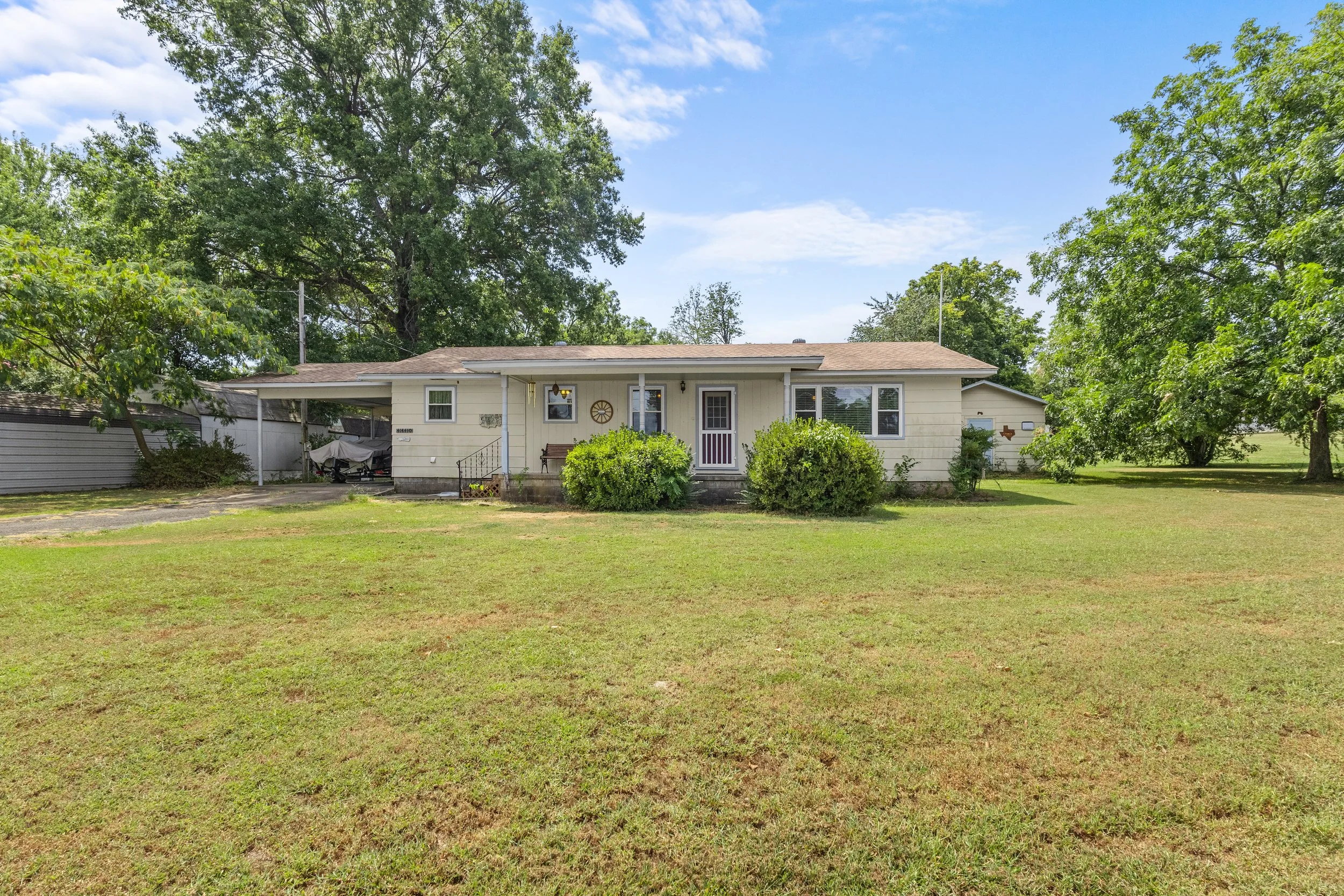 A suburban house with white siding, front porch, and a small set of steps leading to the front door, surrounded by a lawn with trees and bushes, under a partly cloudy blue sky.