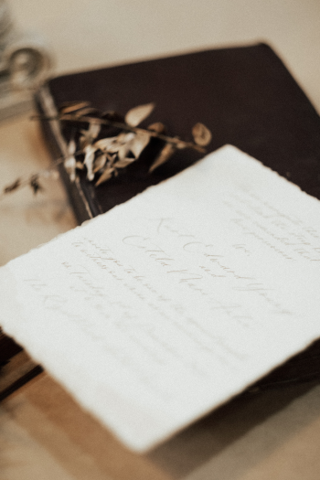 A handwritten letter on a slightly curled piece of paper, placed on top of closed books, with dried flowers nearby.