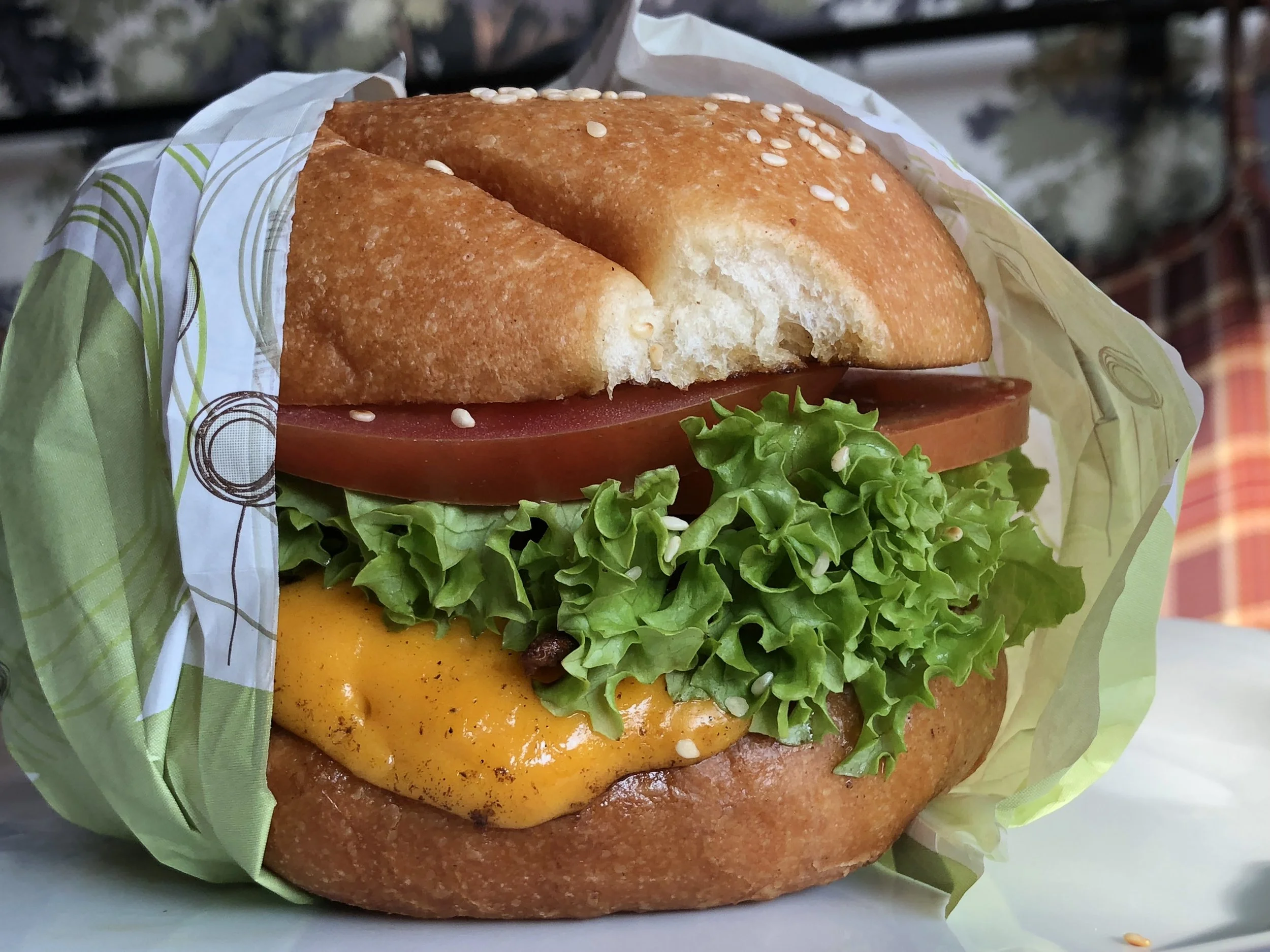 Close-up of a cheeseburger with lettuce, tomato, and cheese in a sandwich bun, partially wrapped in paper.