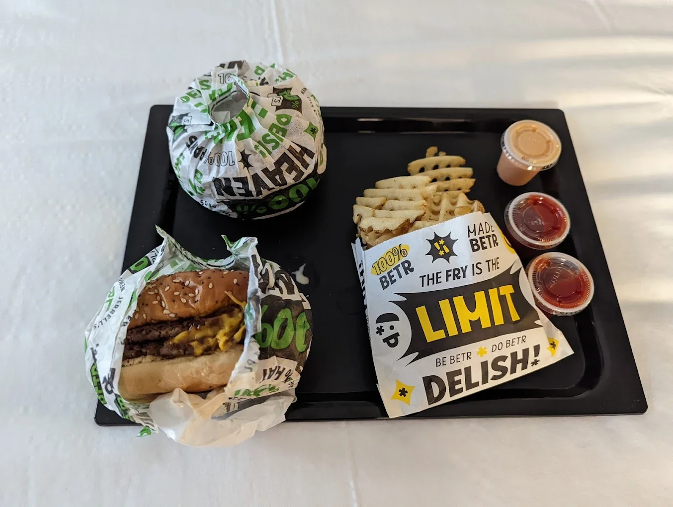 Fast food tray with burger, fries, a wrapped item, and three dipping sauces. Plus a paper with colorful text and graphics.