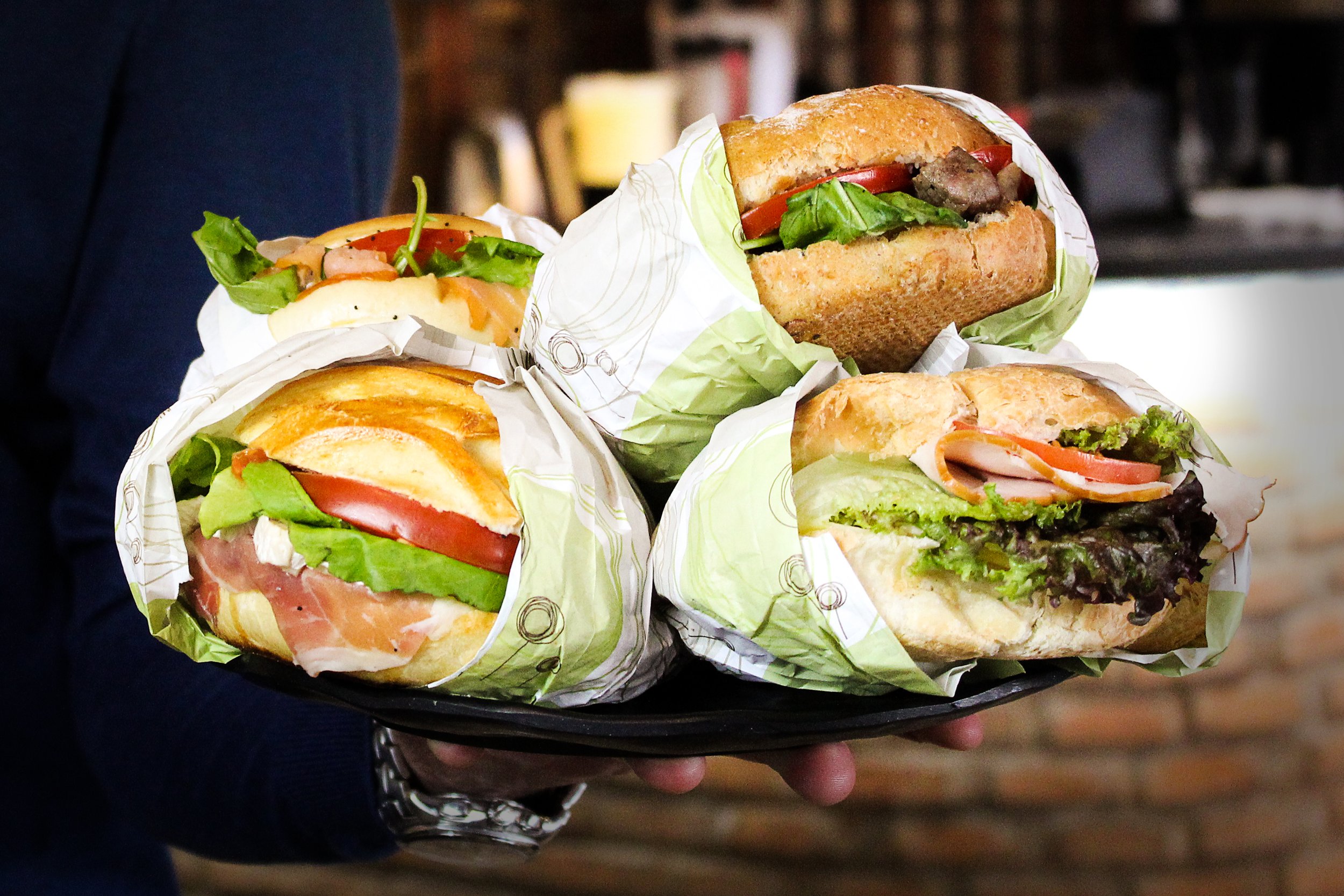Tray of four assorted sandwich wraps with various meats and vegetables on parchment paper.