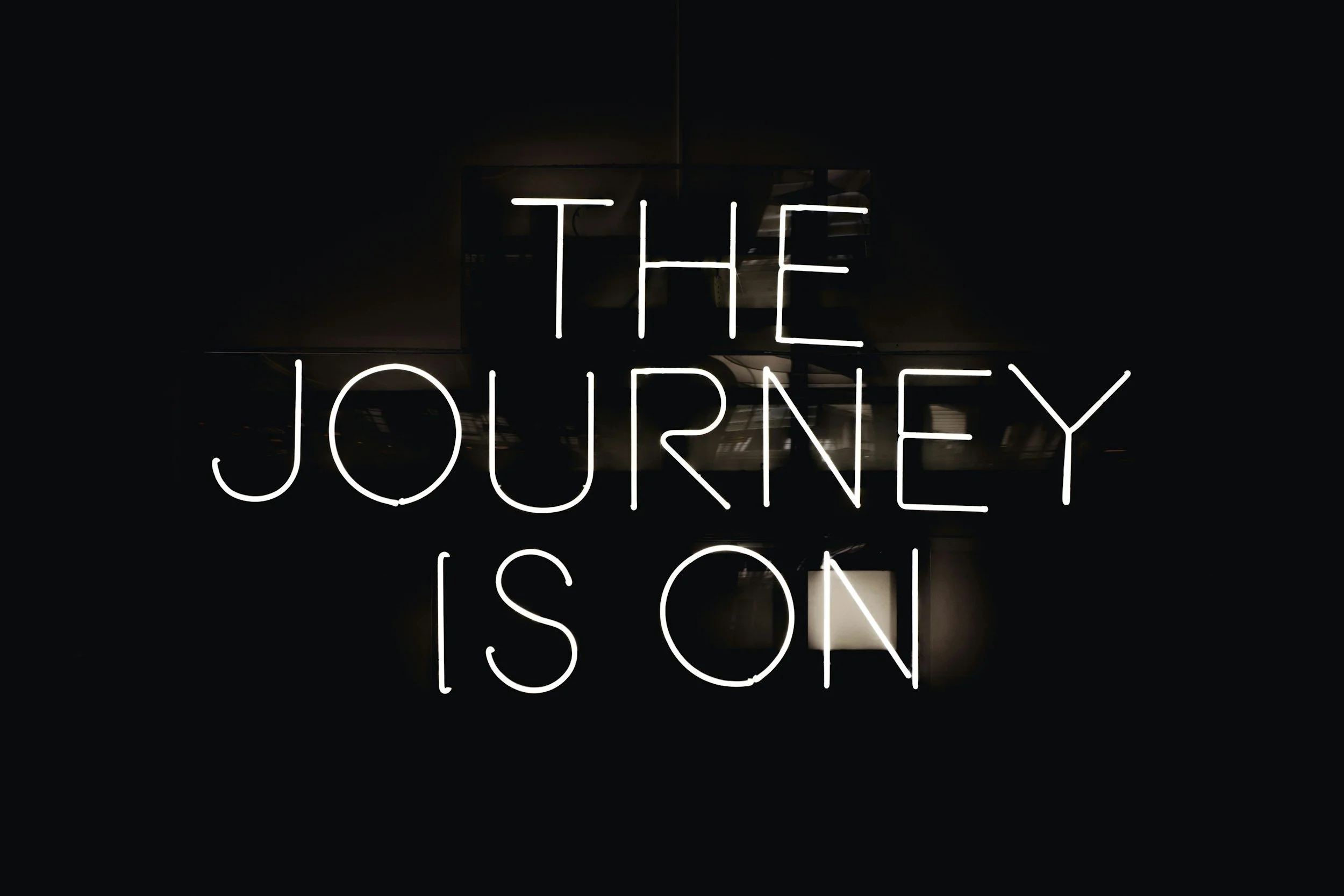 Neon sign with the text 'The Journey Is On' in white against a dark background.