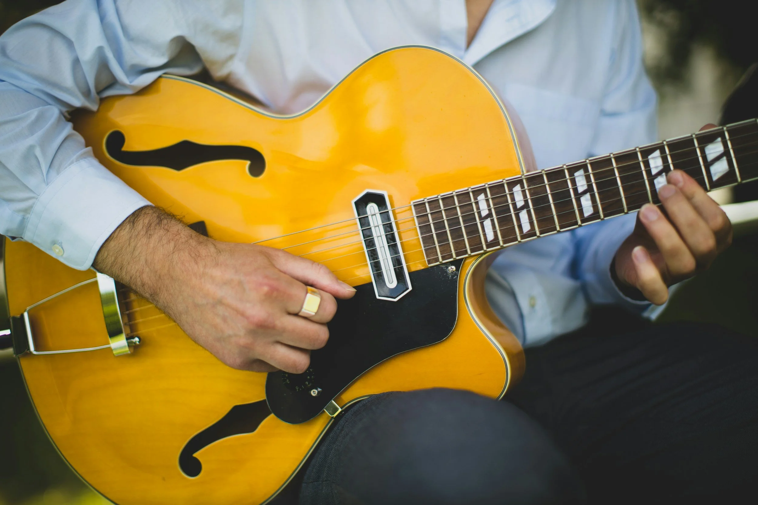 Person playing a yellow acoustic guitar outdoors, visible hands and part of body, wearing a white shirt.