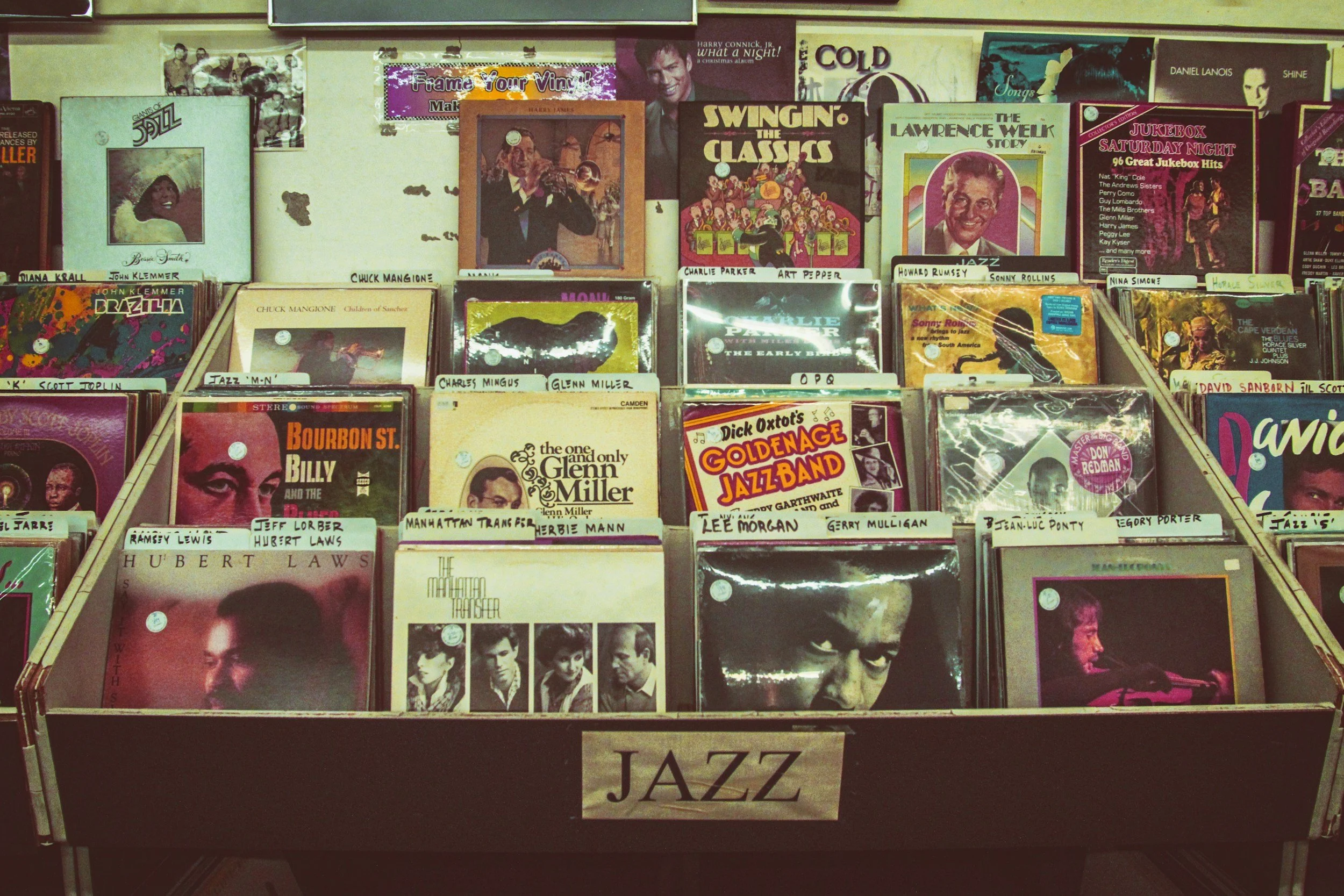 A display of various jazz vinyl records in a record store with a label reading 'JAZZ' on the front of the bin.