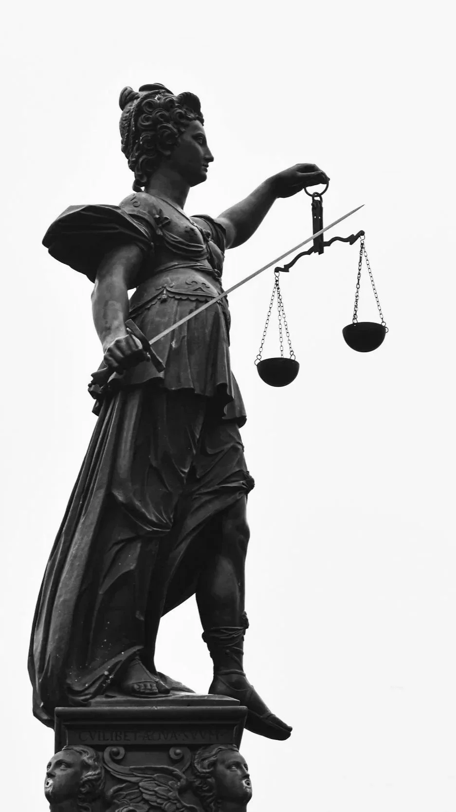 Black and white photograph of a statue of Lady Justice holding scales in her left hand and a sword in her right hand, standing on a pedestal with lion heads.
