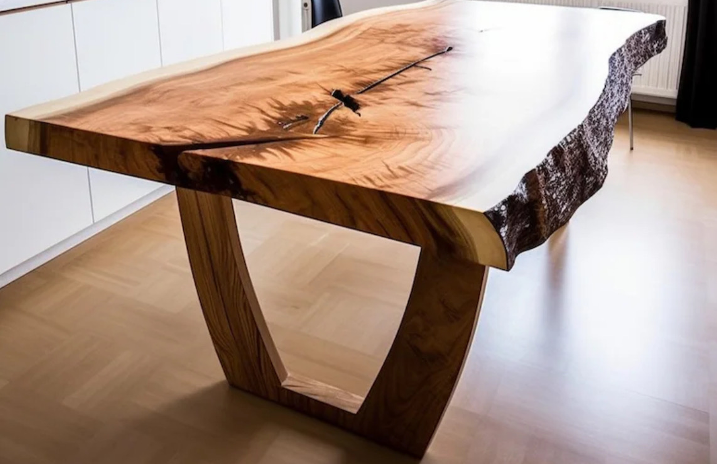 A large wooden table with natural edge, featuring prominent wood grain and a live edge design, supported by curved wooden legs.