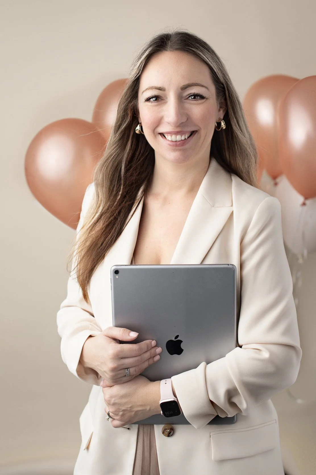 Smiling professional woman holding a laptop in front of rose-gold balloons, captured during a modern personal branding photoshoot by Agata Powers Photography in Orlando.