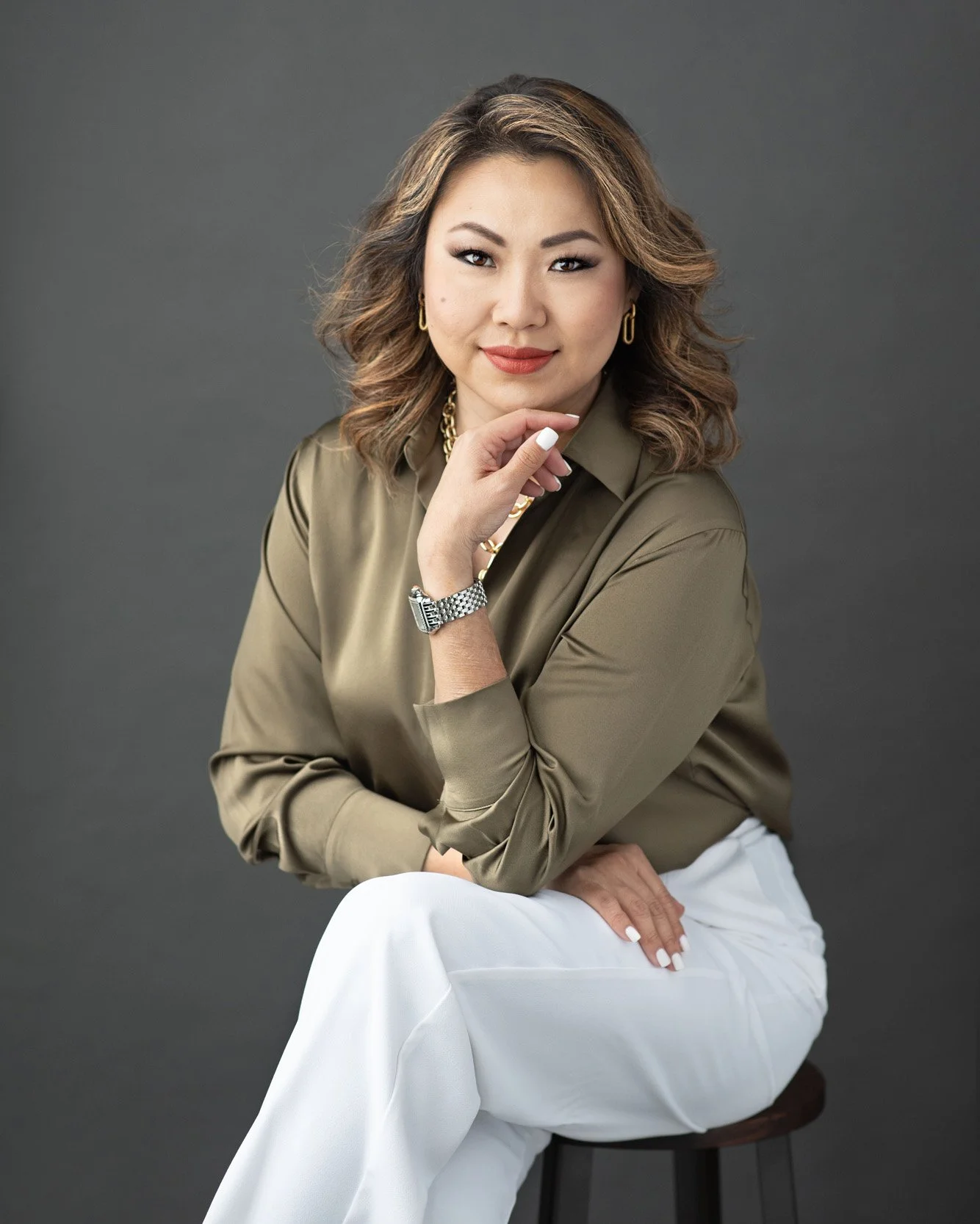 Confident professional woman in a khaki blouse and white pants posing with poise for a modern headshot by Agata Powers Photography, capturing strength and approachability for personal branding.