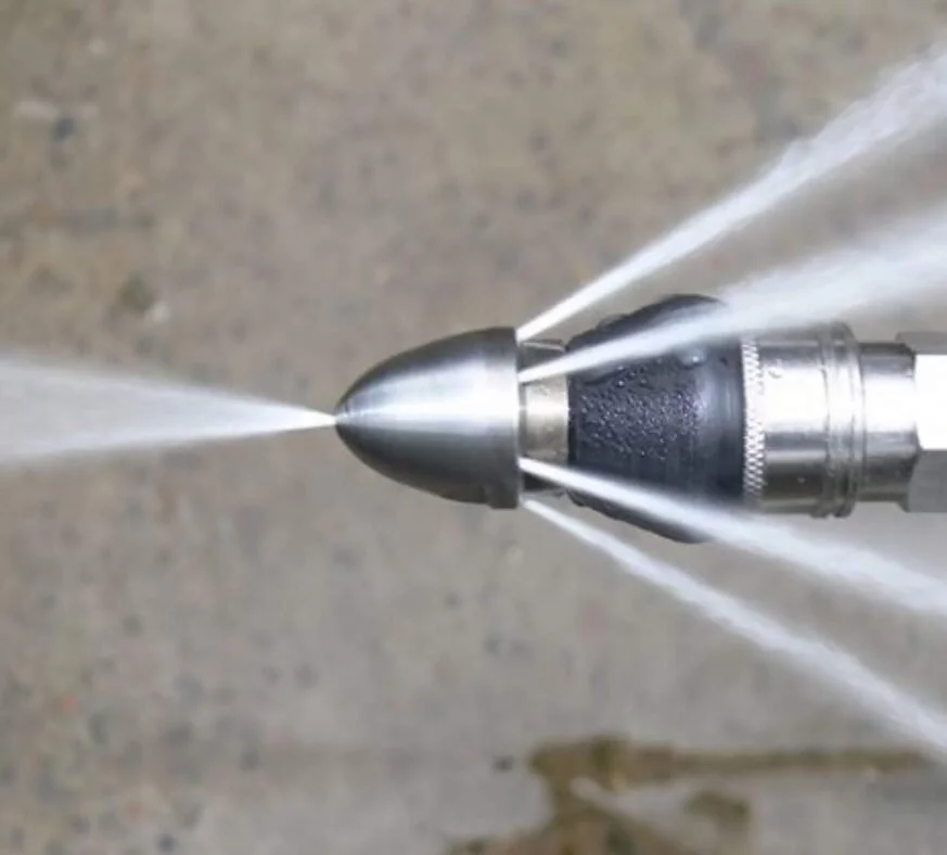 A close-up of a metal nozzle spraying water in four directions.