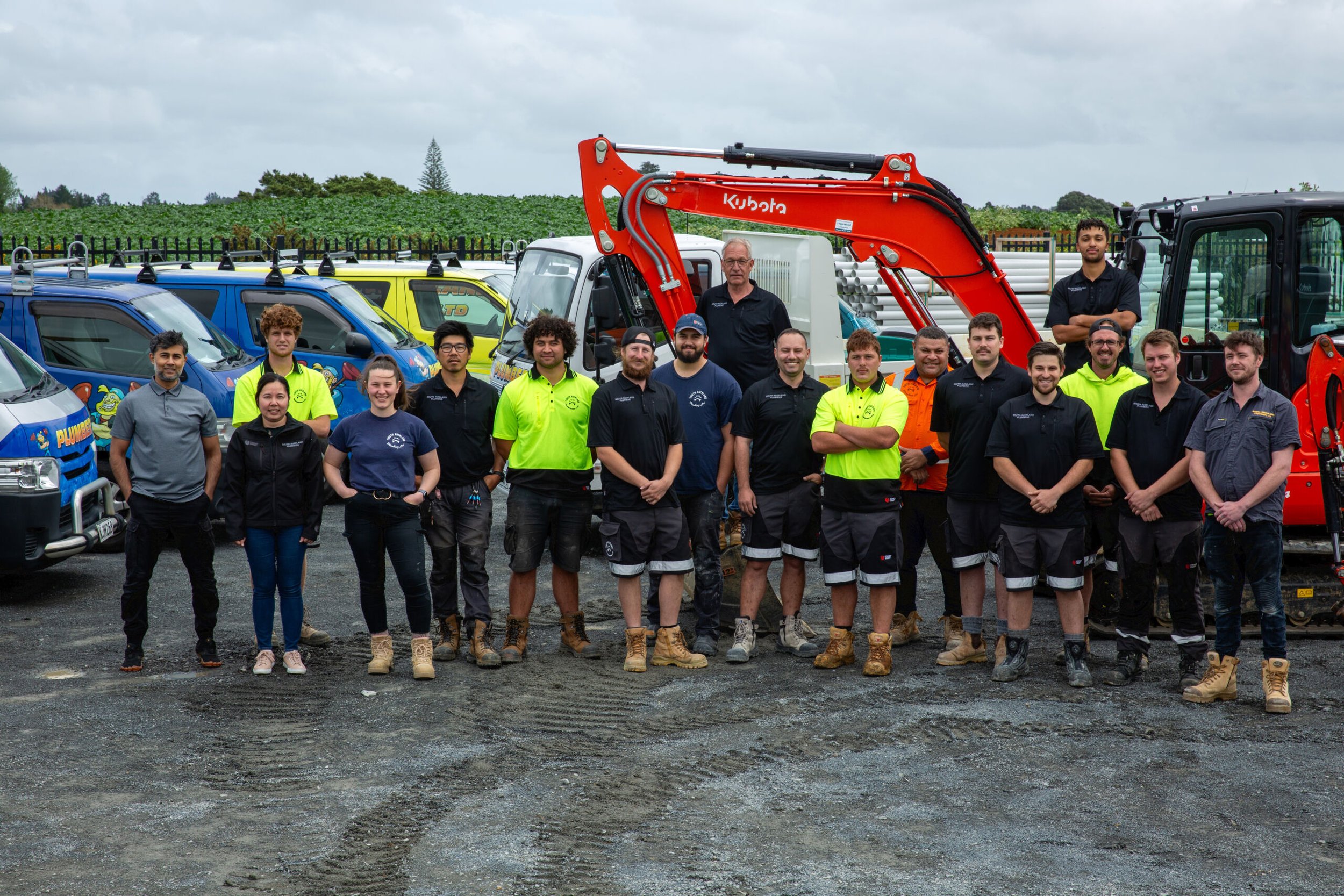 Grantham Group team of workers standing outdoors in front of utility vehicles and construction equipment. The sky is cloudy and the background features green fields.