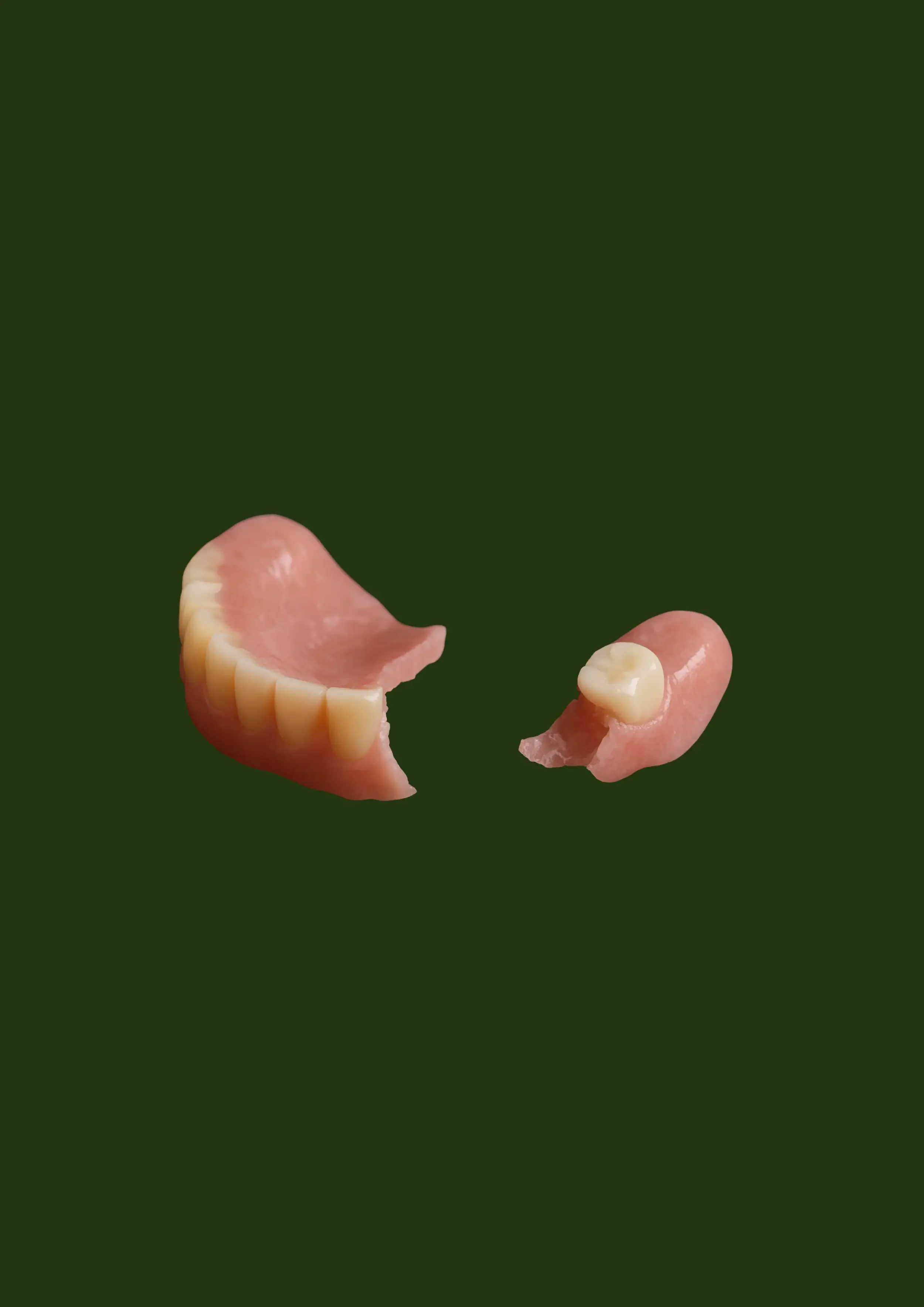 Complete upper and lower dentures broken in half on dark green background — Prestige Dentures Auckland