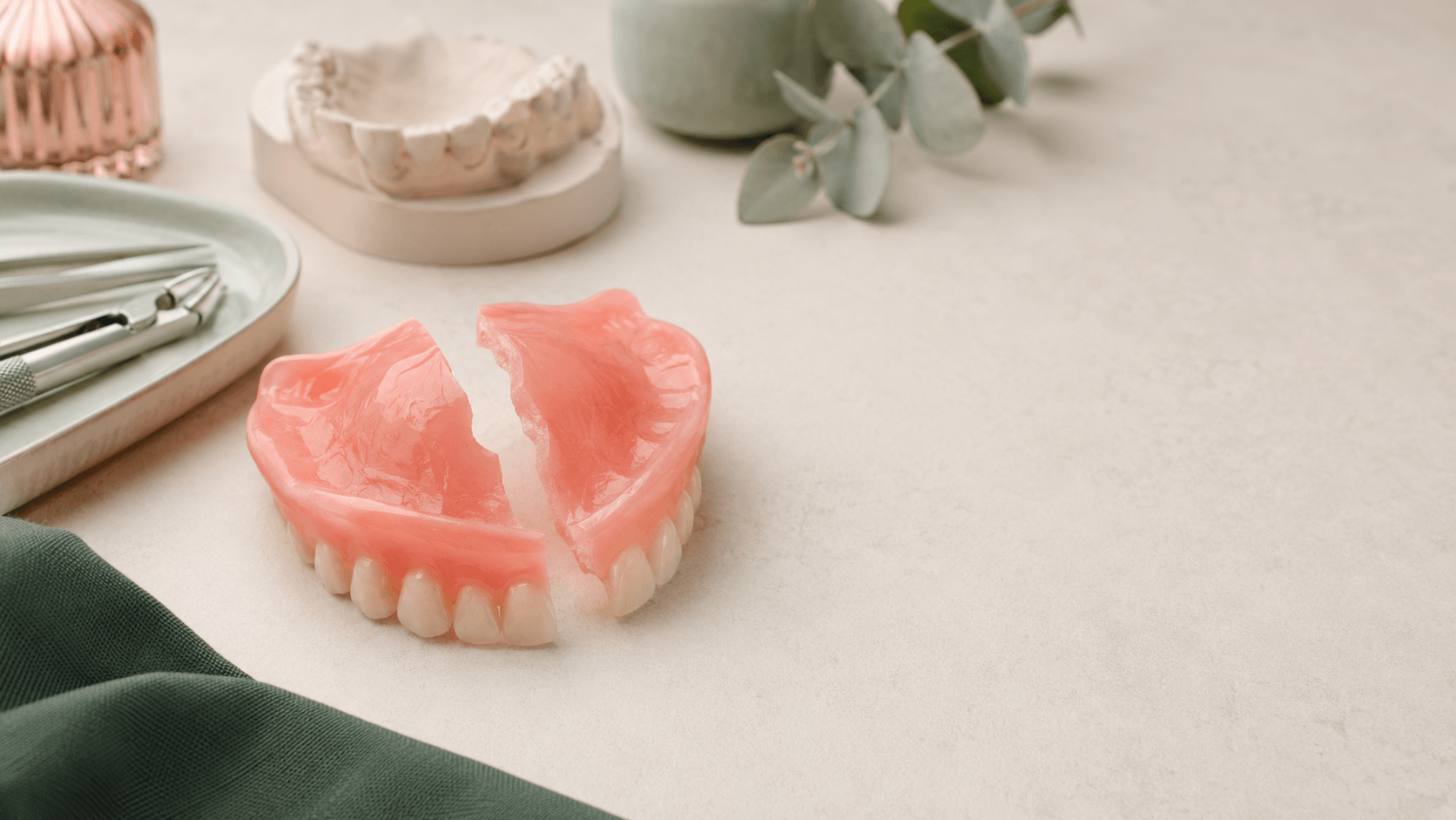 Complete upper dentures broken in half on dark green background — Prestige Dentures Auckland