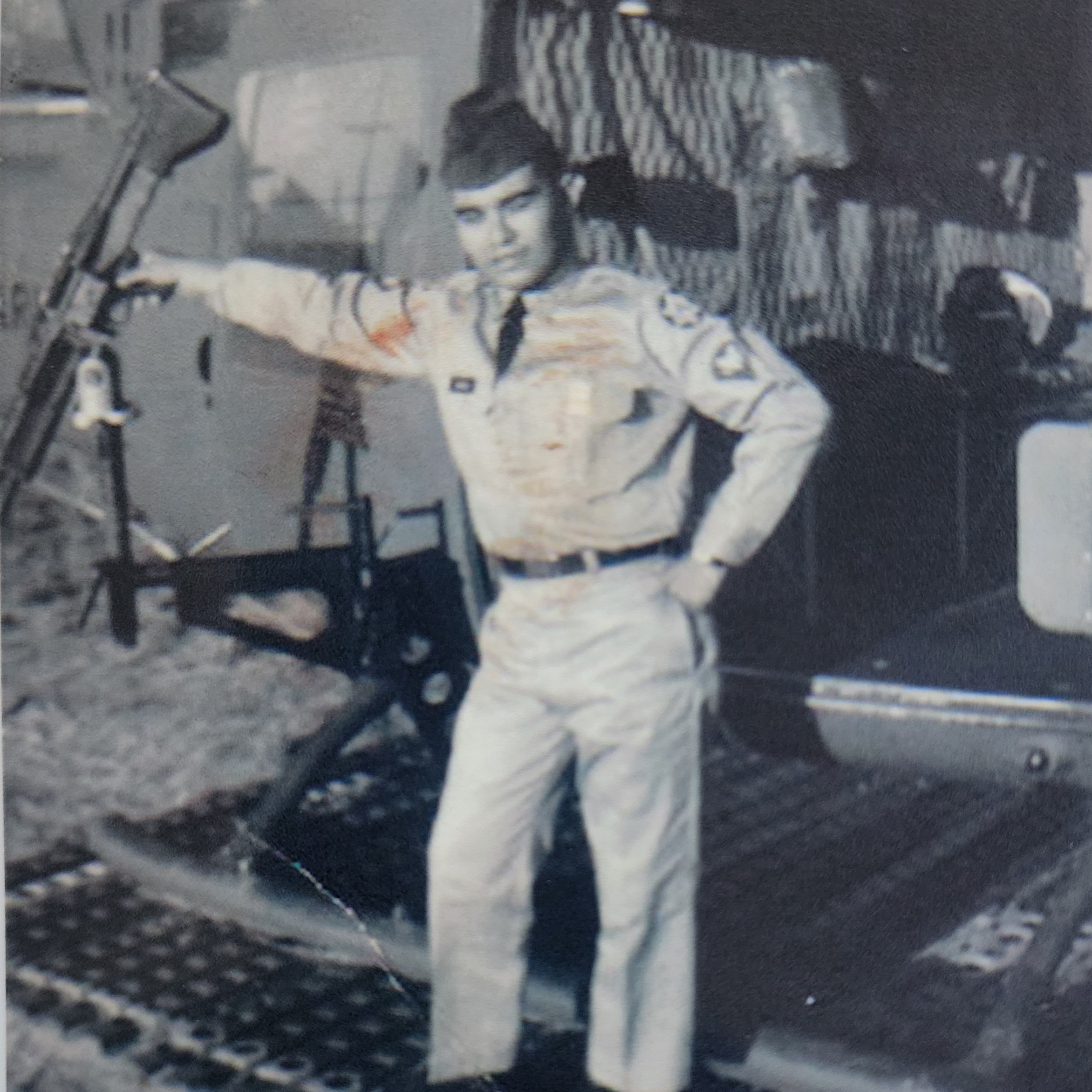 A man dressed in a vintage military pilot uniform, standing next to an aircraft, with one hand on his hip and the other resting on the aircraft's propeller.