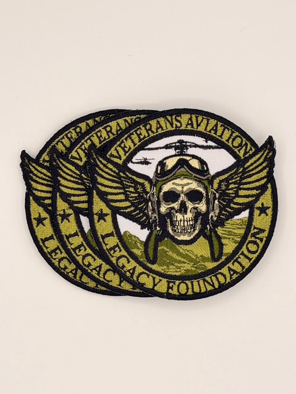 Stack of olive-green Veterans Aviation Legacy Foundation patches featuring pilot skull and golden wings design.