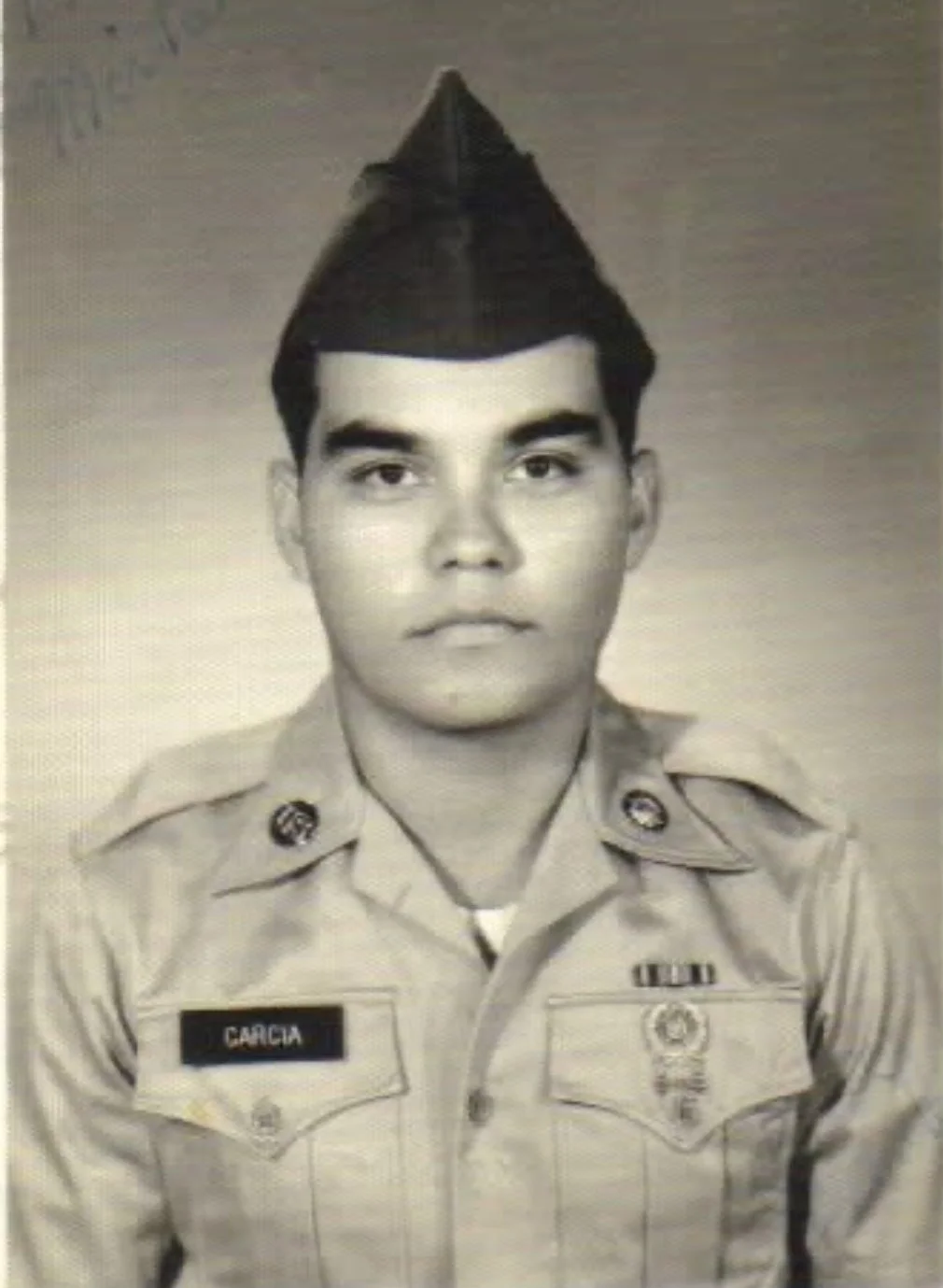 Black and white photo of a young military man in uniform with a name tag 'GARCIA' and patriotic medals, wearing a cap.