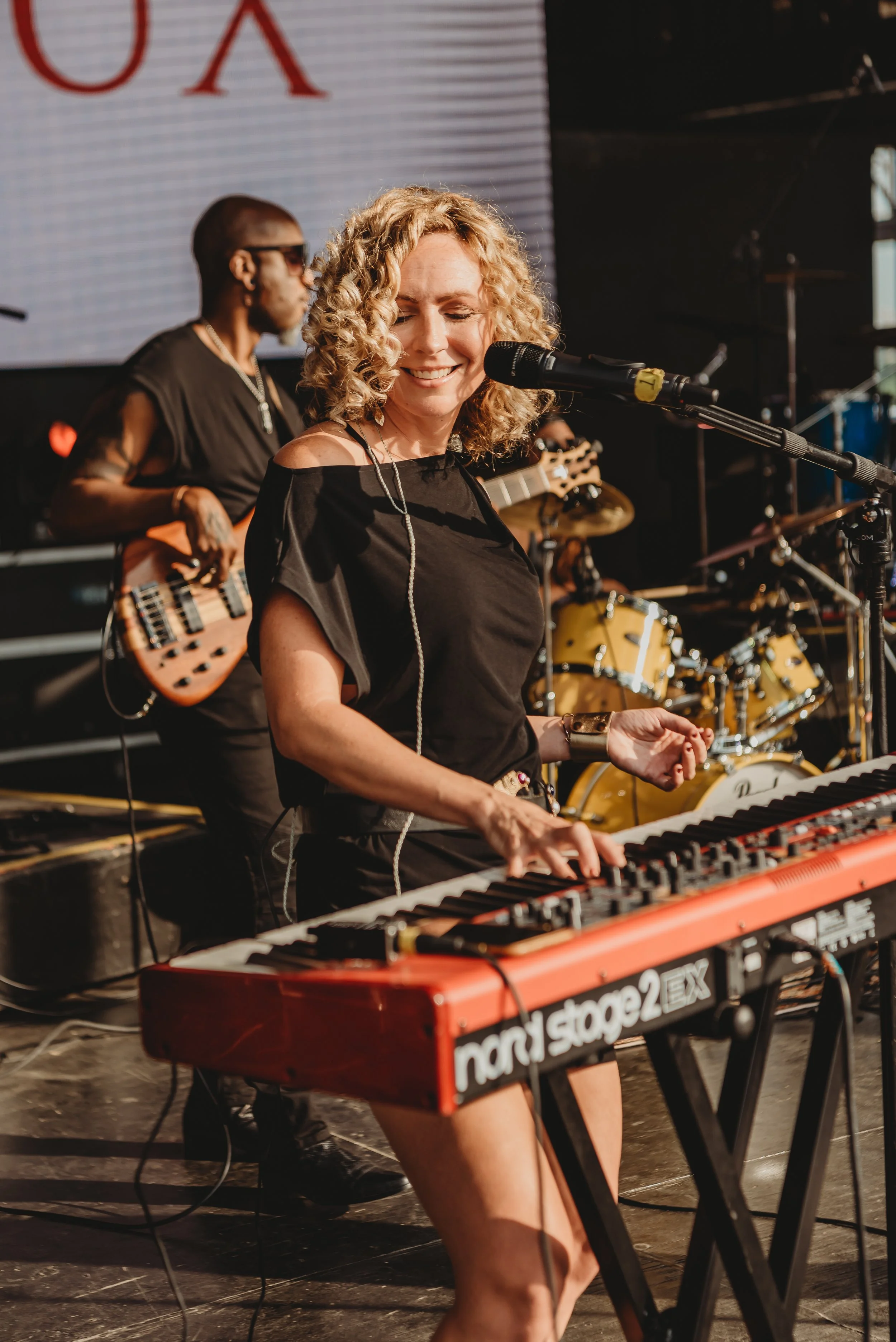 Leora Nosko standing at the microphone.  Playing with the band The Roux.  Performing at Jeffersonville, Indiana Riverstage.  Playing Nord keyboard and singing.