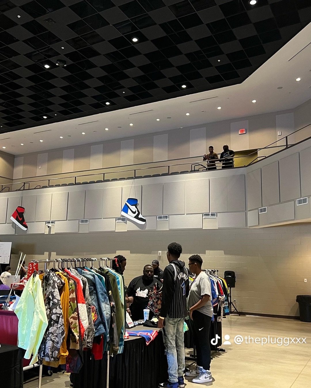 Indoor sneaker and clothing sale event with multiple people browsing, hanging sneakers on display, and a two-story venue with seating and logos of Nike and Jordan.