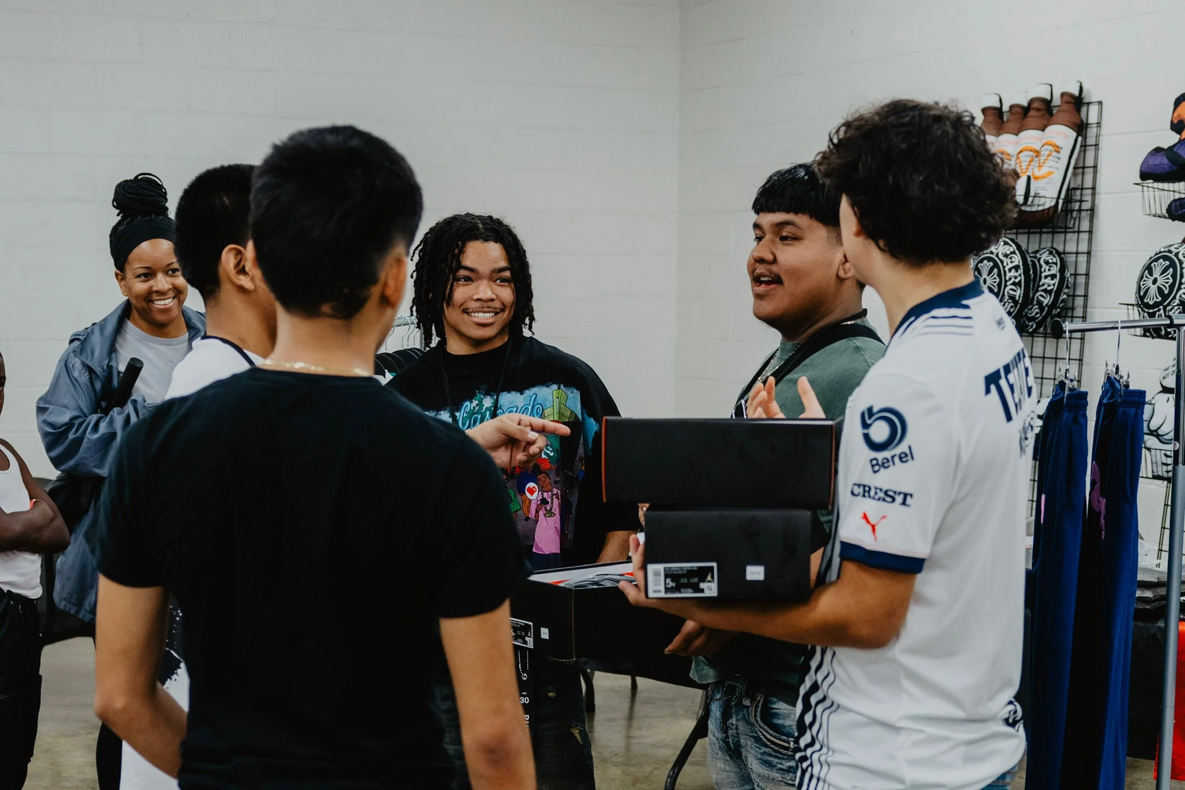 Group of young people, some holding shoeboxes, engaging in conversation inside a store with sports shoes and apparel on display.
