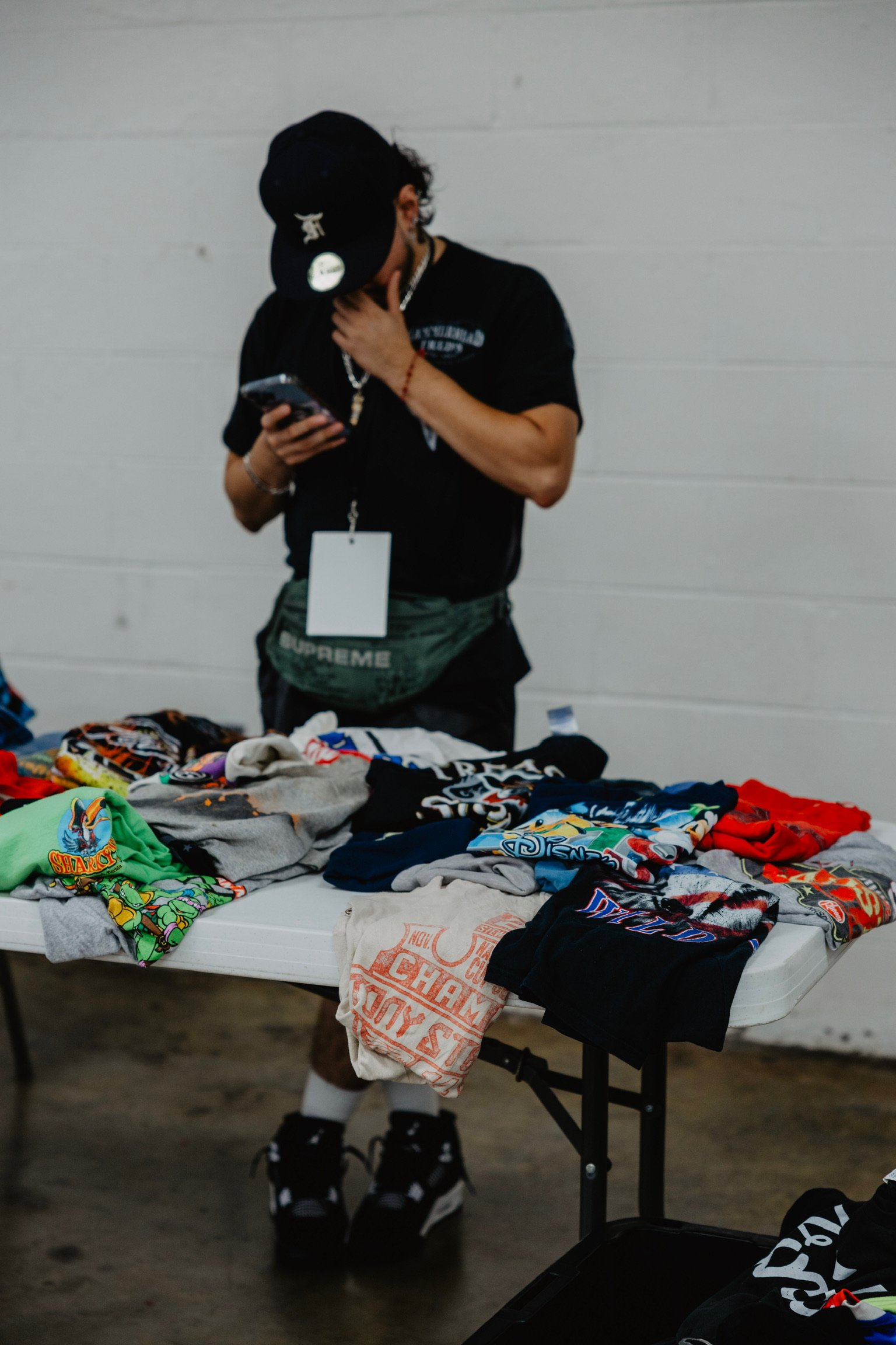 A person browsing colorful T-shirts displayed on a table, with some T-shirts hanging on the side, in an indoor setting.