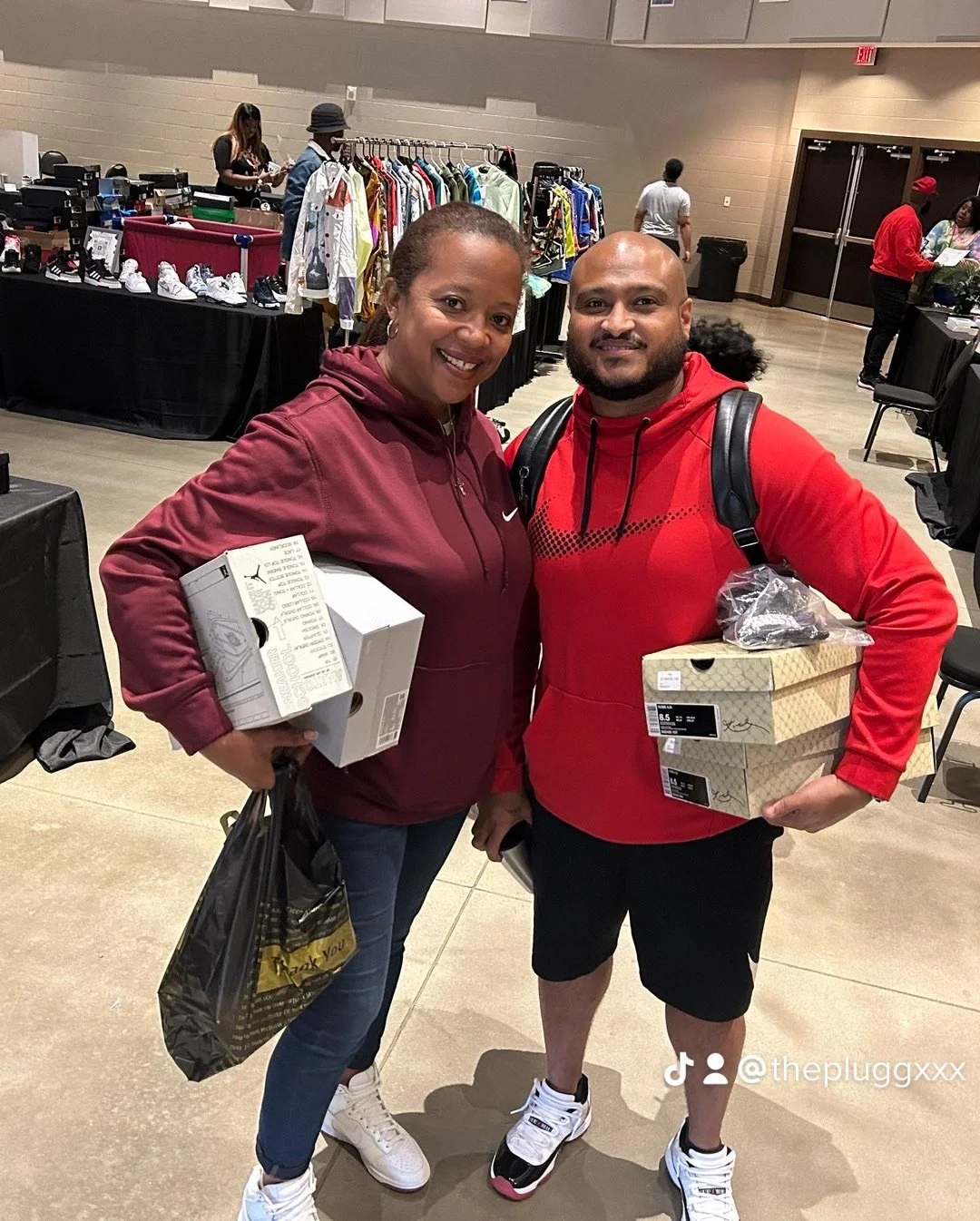 Two smiling people standing inside a store, each holding shoe boxes and shopping bags, with clothing and shoes displayed in the background.