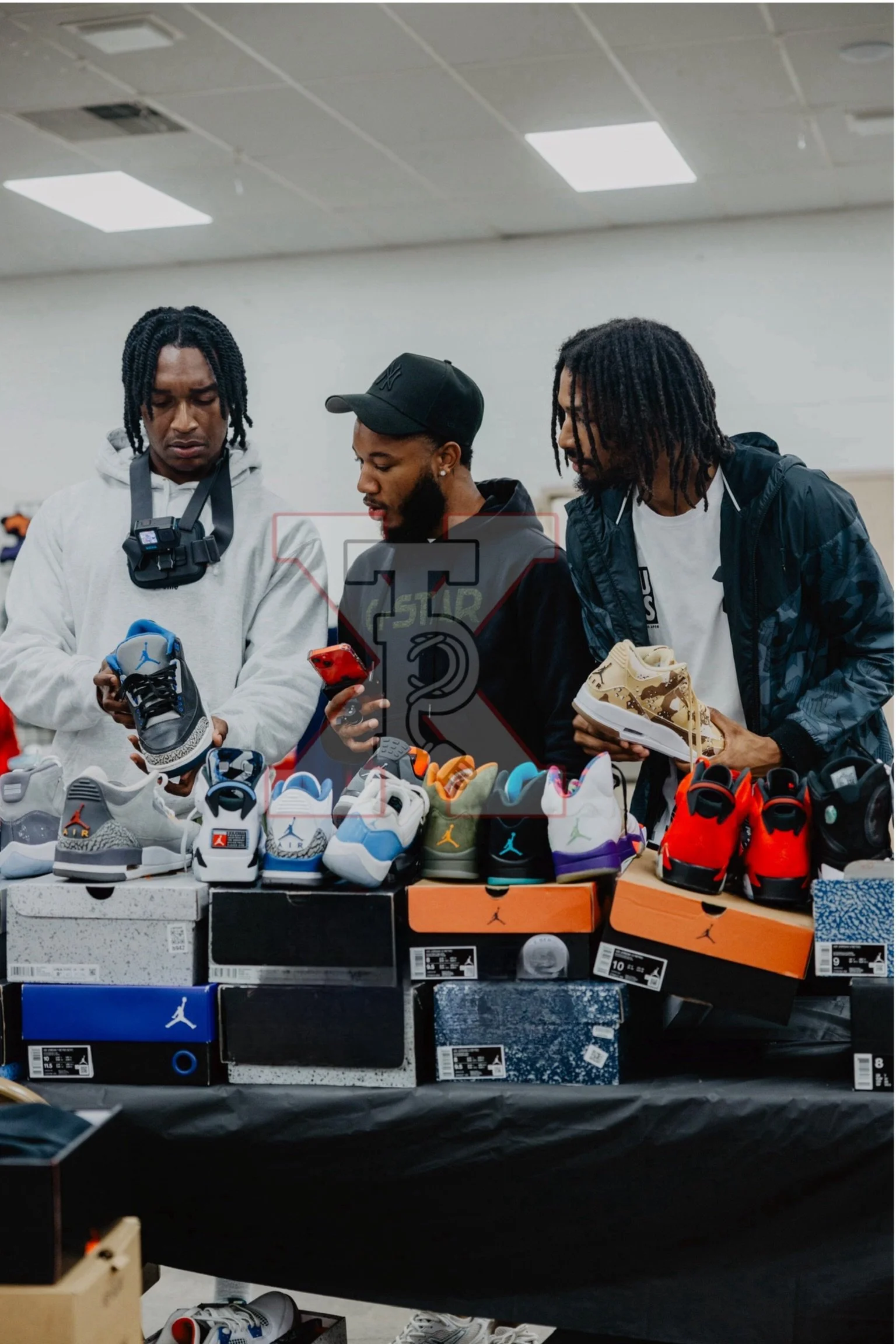 Three young men browsing sneakers displayed on a table at a shoe sale.