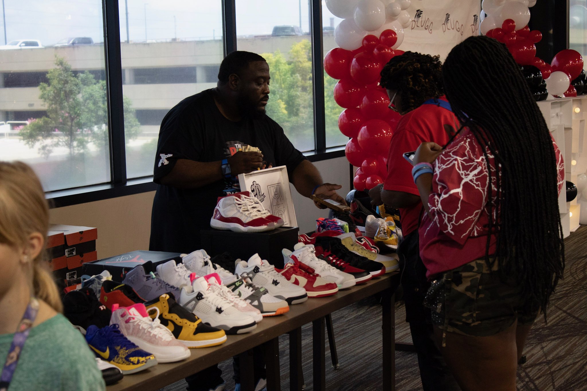 People shopping for sneakers at a booth with a variety of colorful athletic shoes displayed on a table, decorated with red, white, and black balloons.
