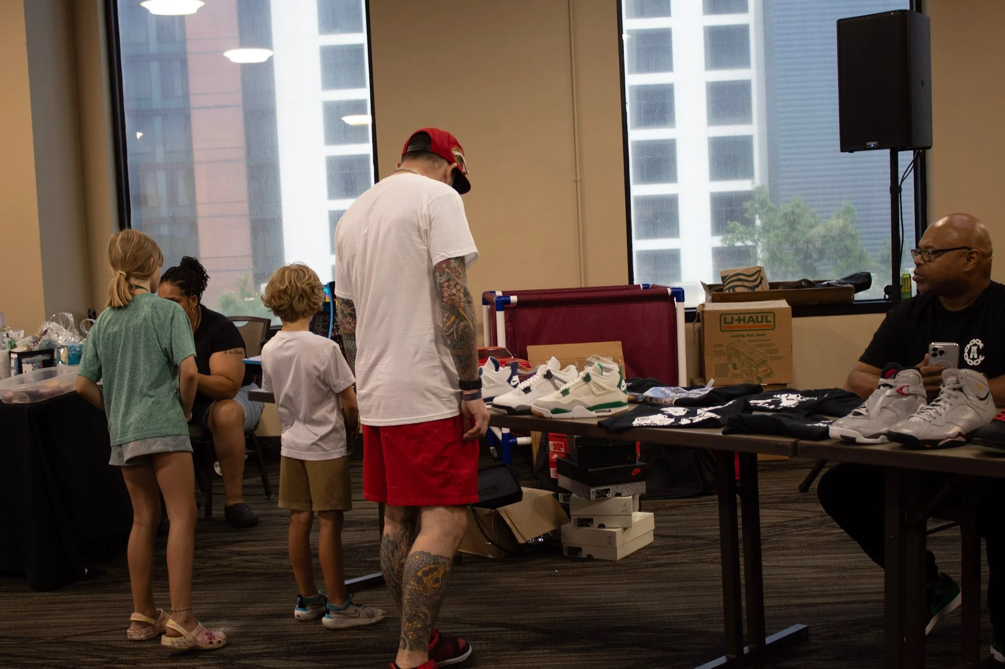 People shopping for sneakers at an indoor sale event, with tables displaying sneakers and other merchandise.