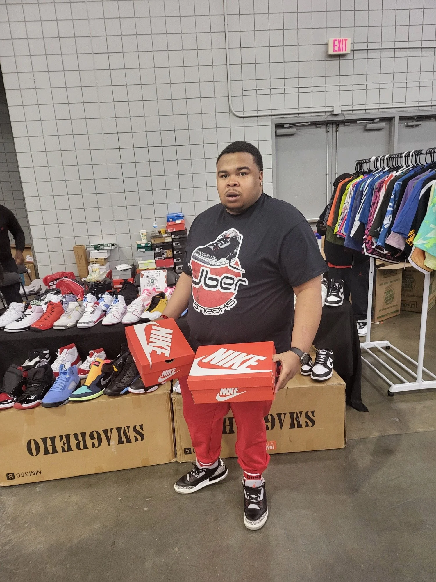 Man standing indoors holding two Nike shoe boxes, surrounded by sneaker display and clothing racks.